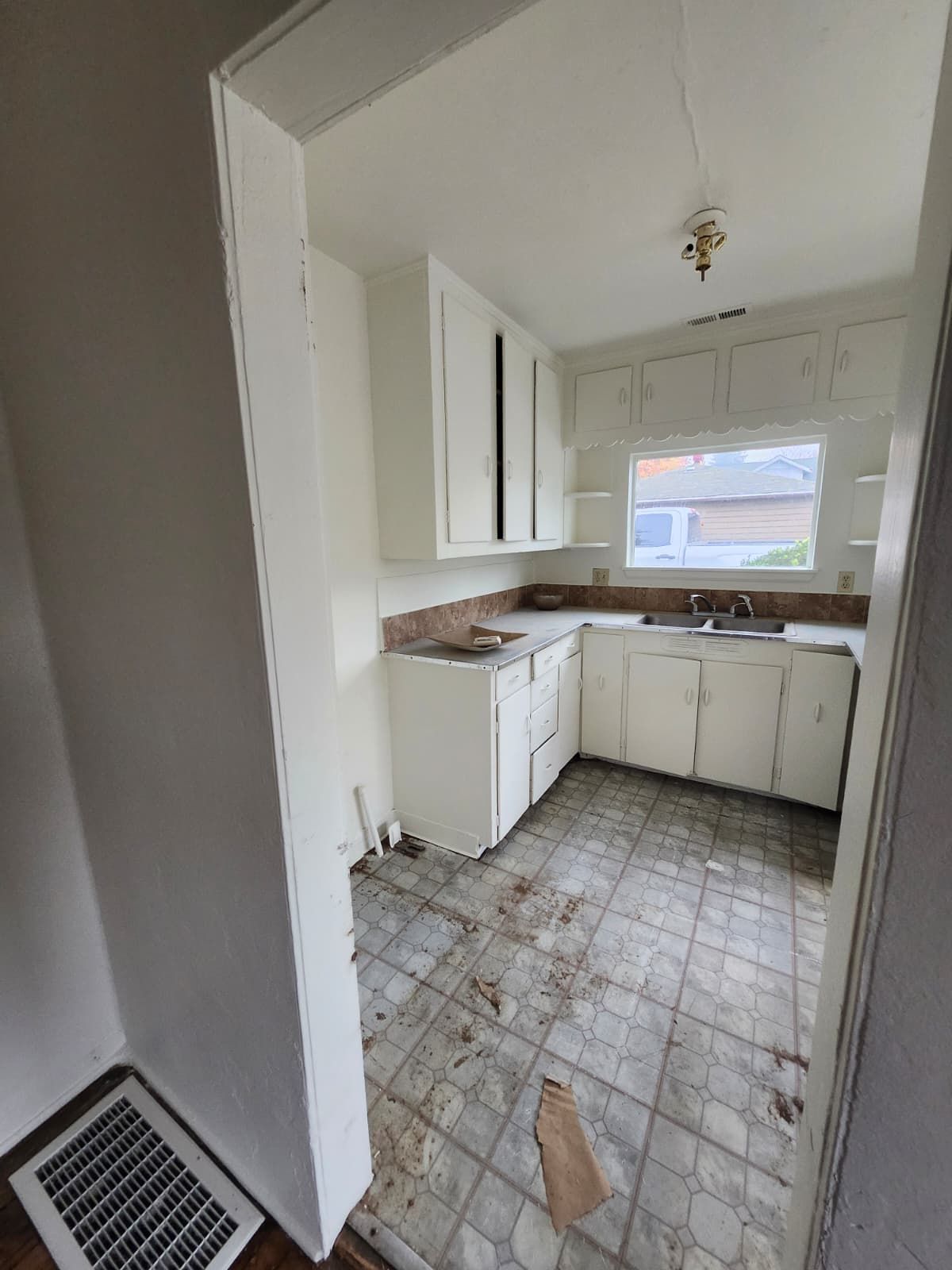 Small, worn kitchen with white cabinets, dirty tiled floor, and a window over the sink