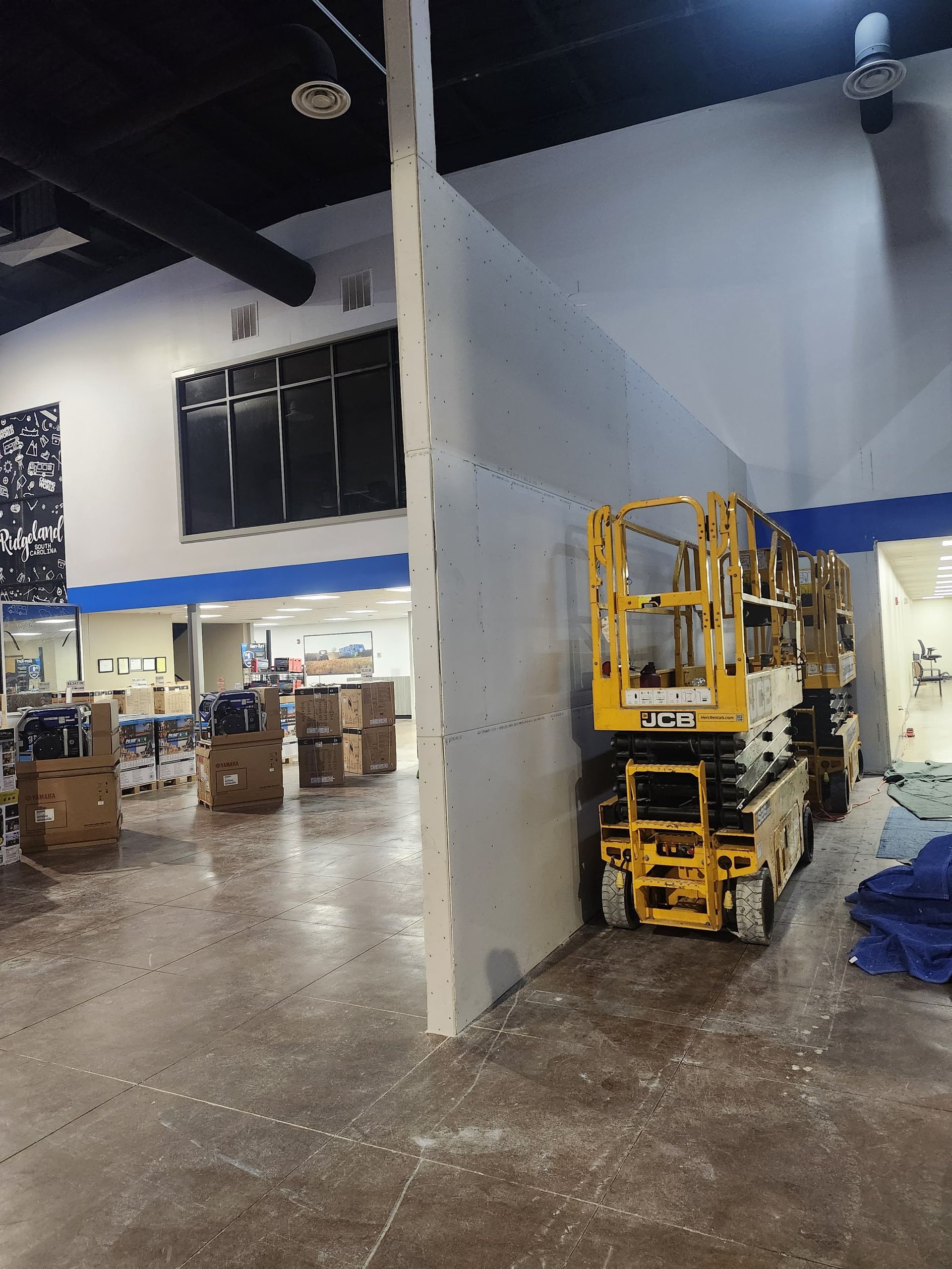 Industrial warehouse interior with yellow scissor lifts beside a white partition wall