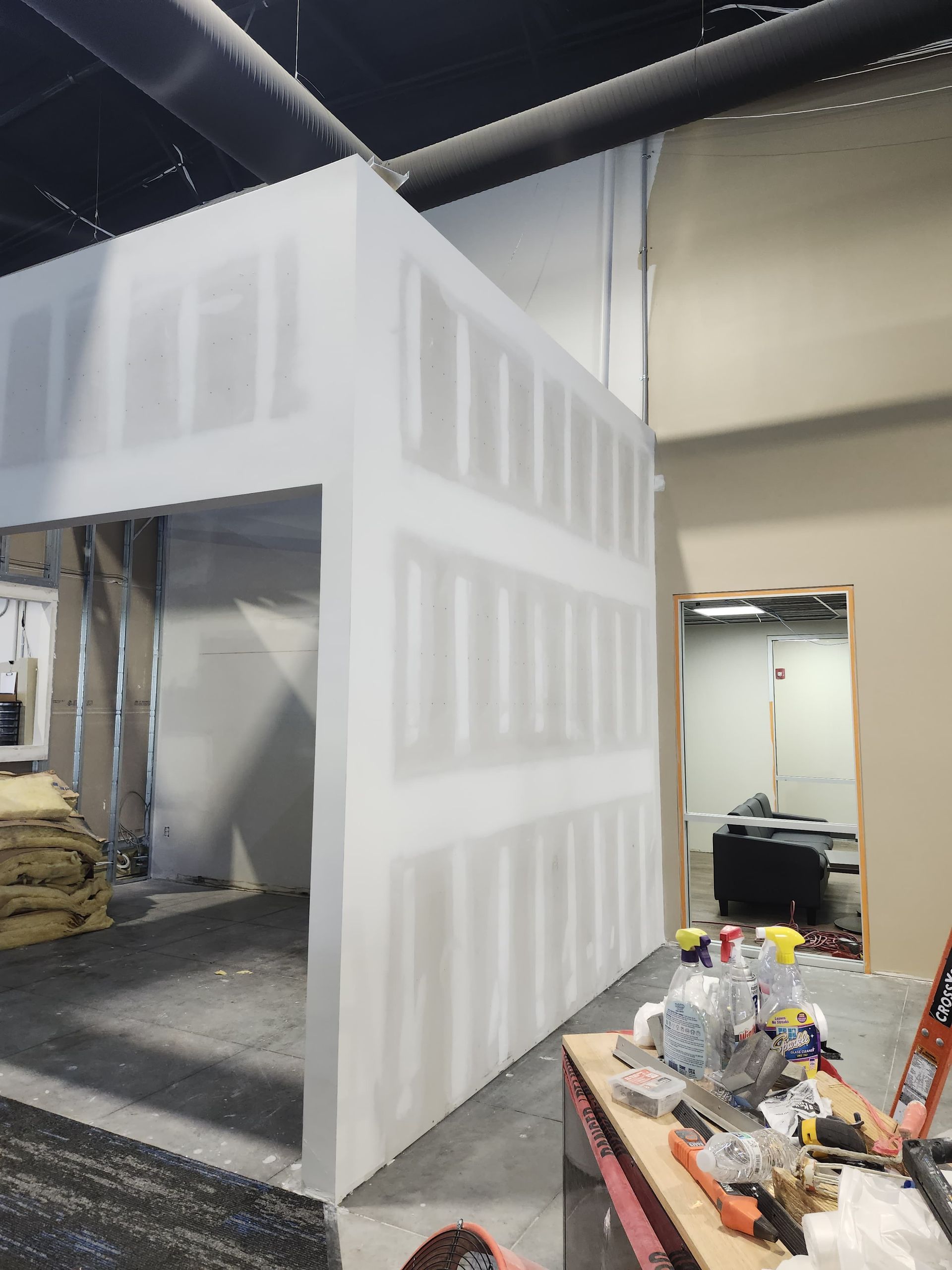 Partially finished drywall booth in a warehouse, with tools and debris on a table nearby