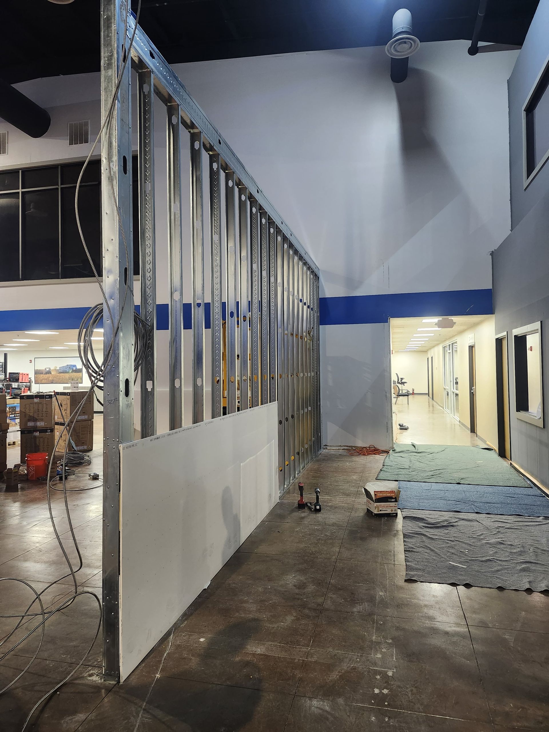 Unfinished interior hallway with exposed studs, white walls, blue stripe, and construction debris on the floor