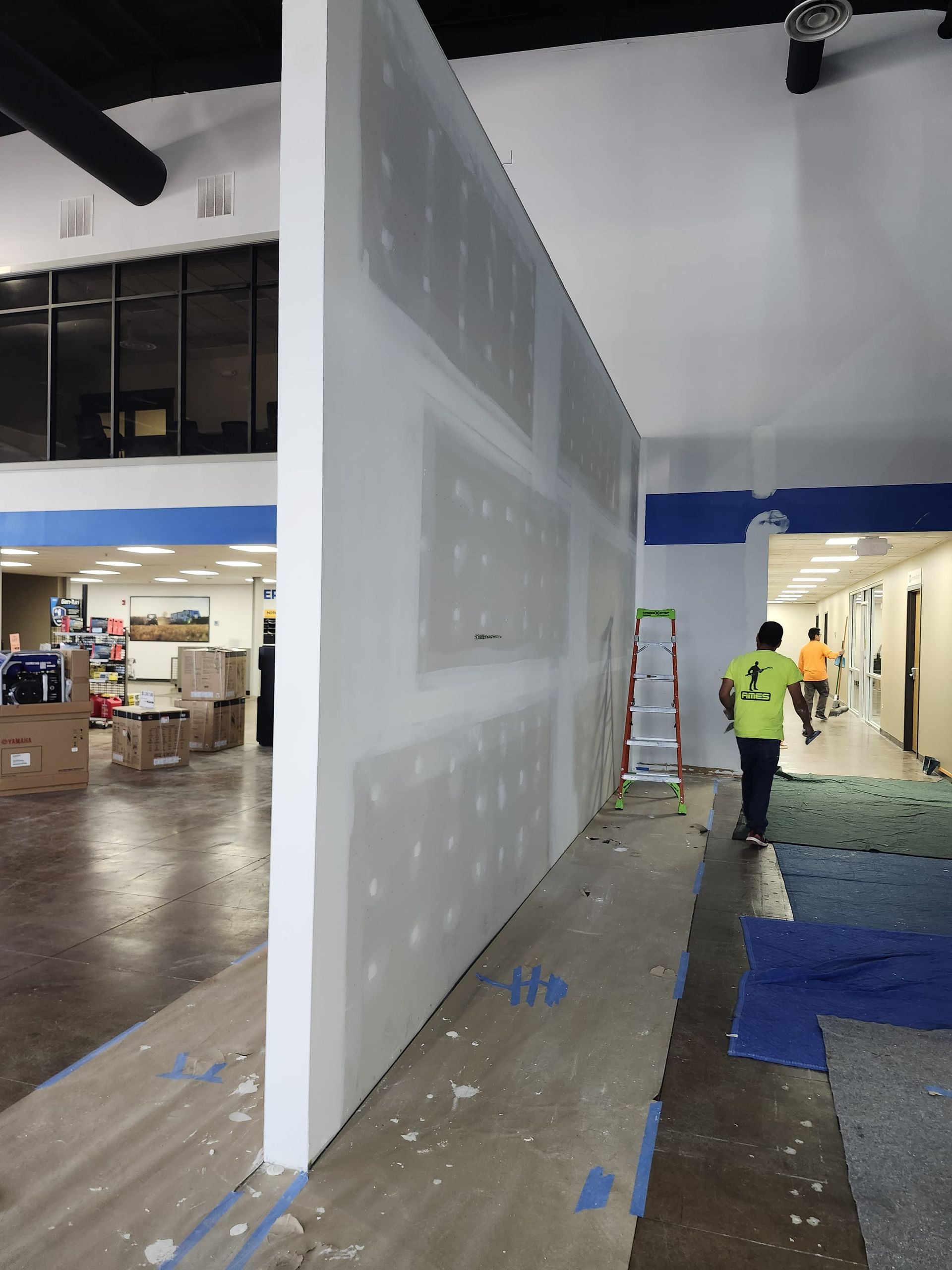 Large white wall panel under construction in a bright indoor hall, with workers and equipment nearby