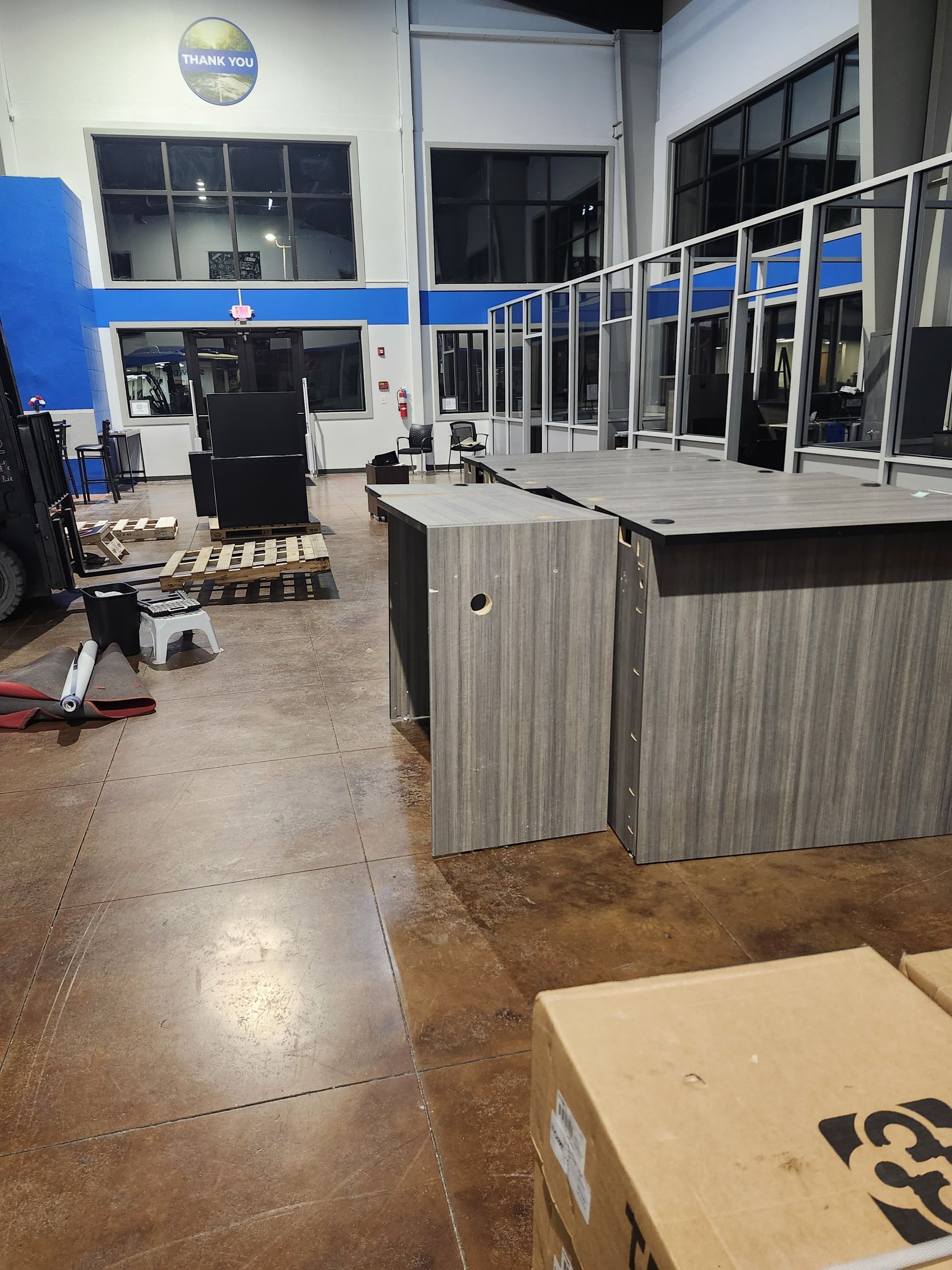 Empty industrial room with metal desks, chairs, and a pallet on a polished concrete floor