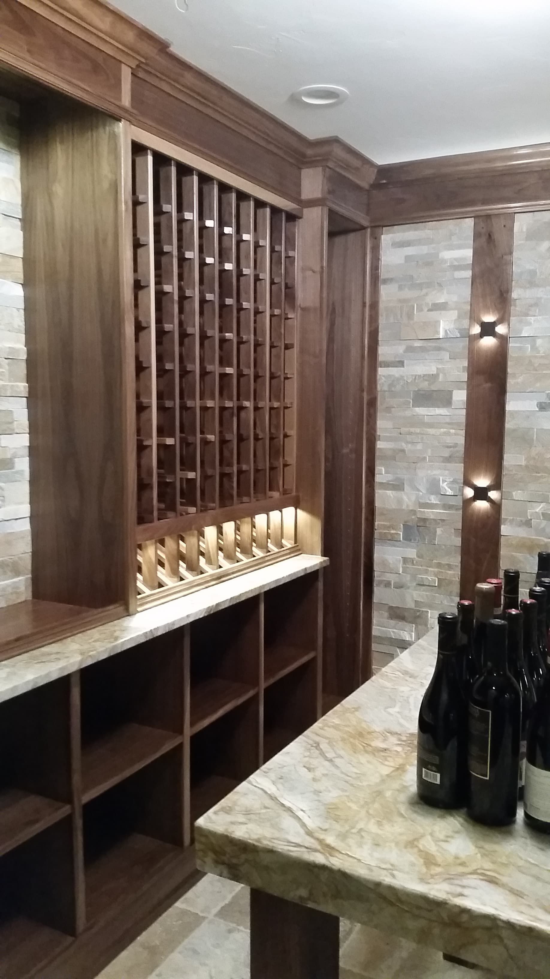 Wine cellar with wooden racks, stone walls, and bottles on a table.