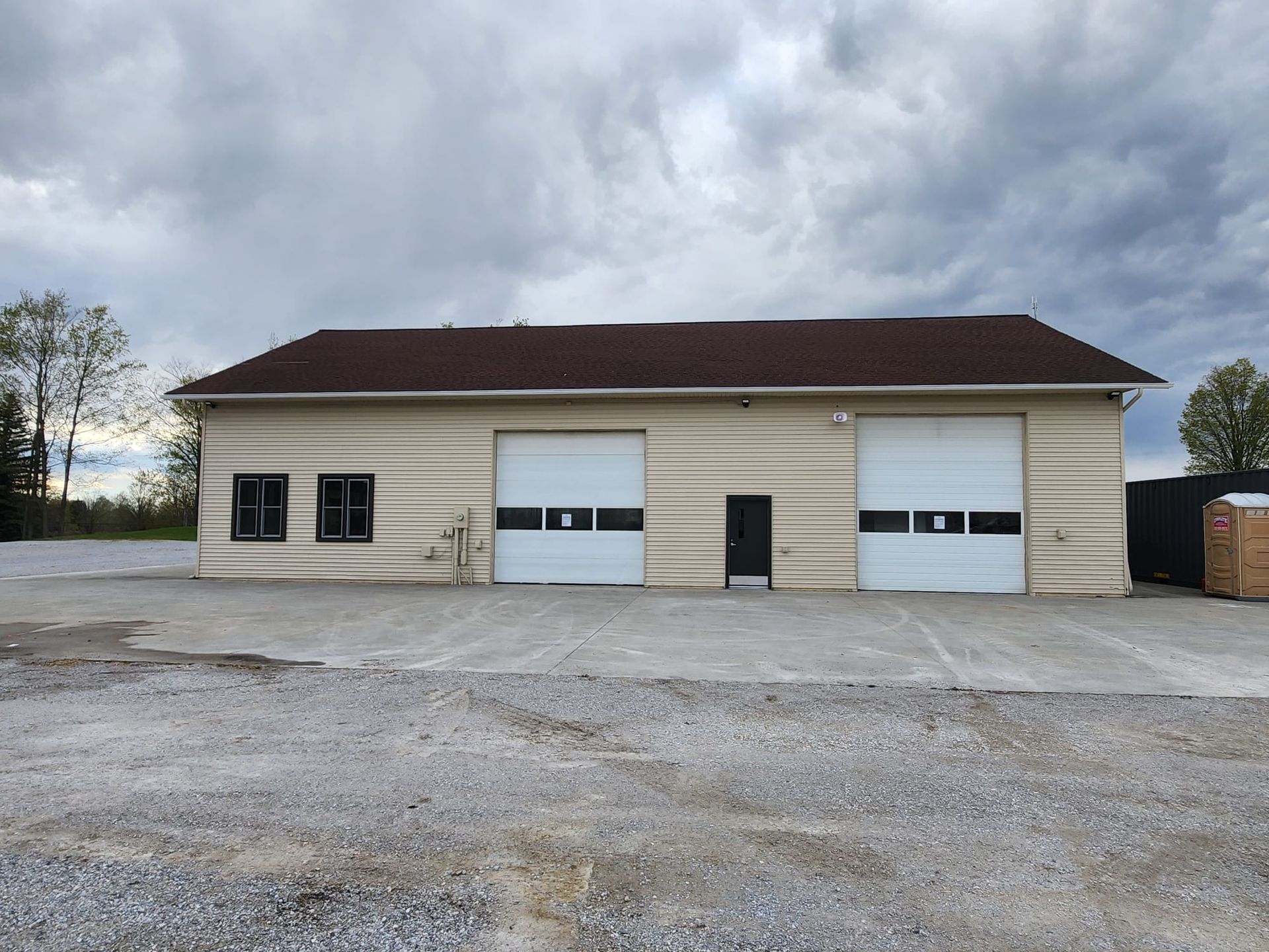 Large beige garage building with two white roll-up doors under a cloudy sky
