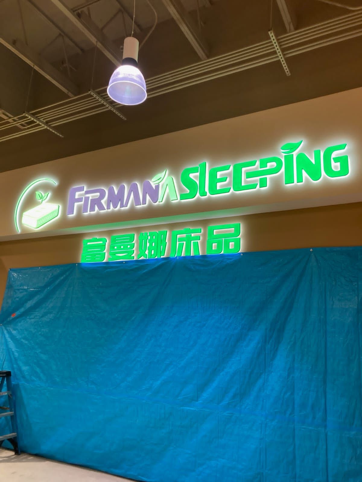 Neon “FRMAN SLEEPING” sign above a large blue tarp in an indoor warehouse-like space