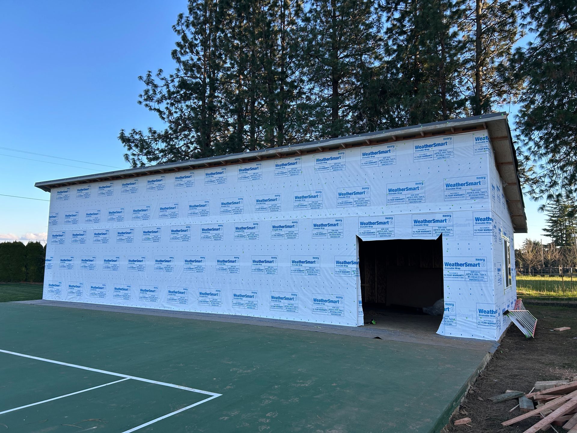 Partially sheathed white building beside an outdoor sports court at dusk