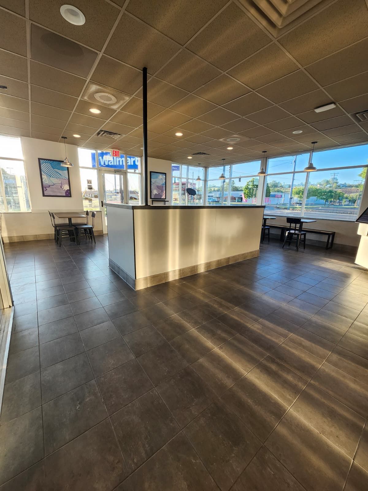 Empty airport lounge with dark flooring, central counter, seating, and large windows overlooking the tarmac