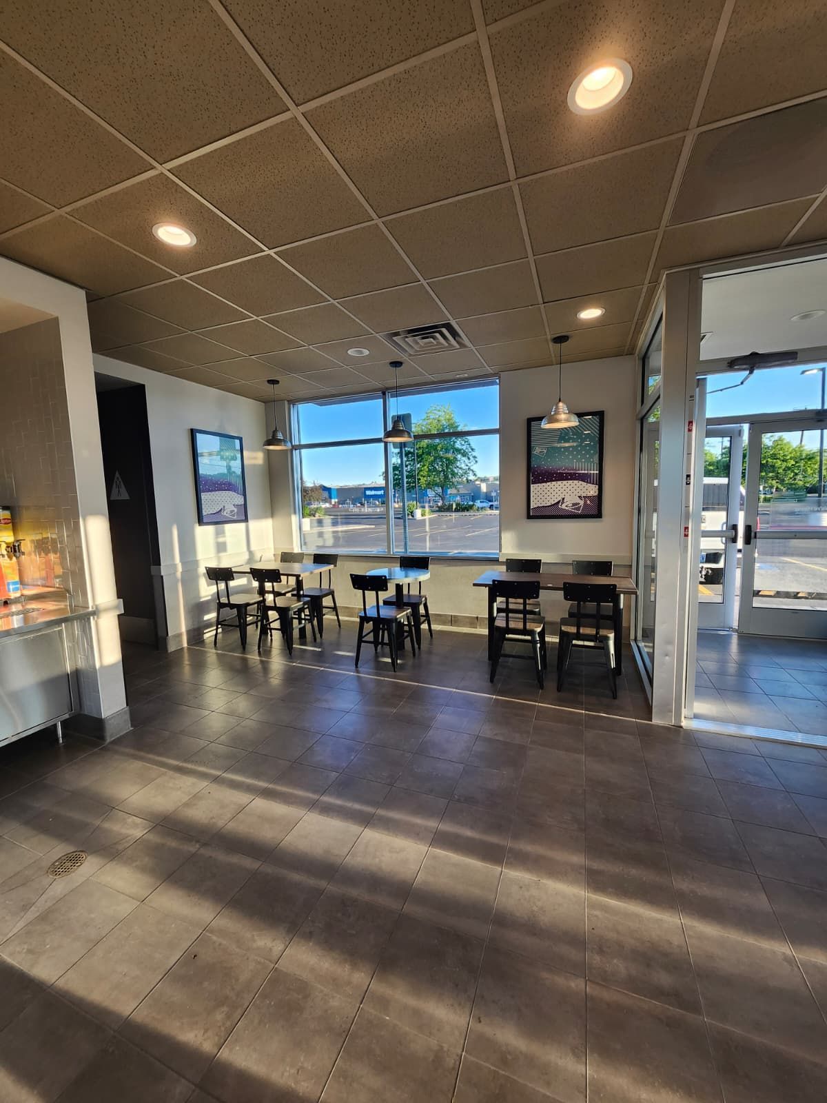 Empty café interior with tables, chairs, and warm lights, facing large front windows.