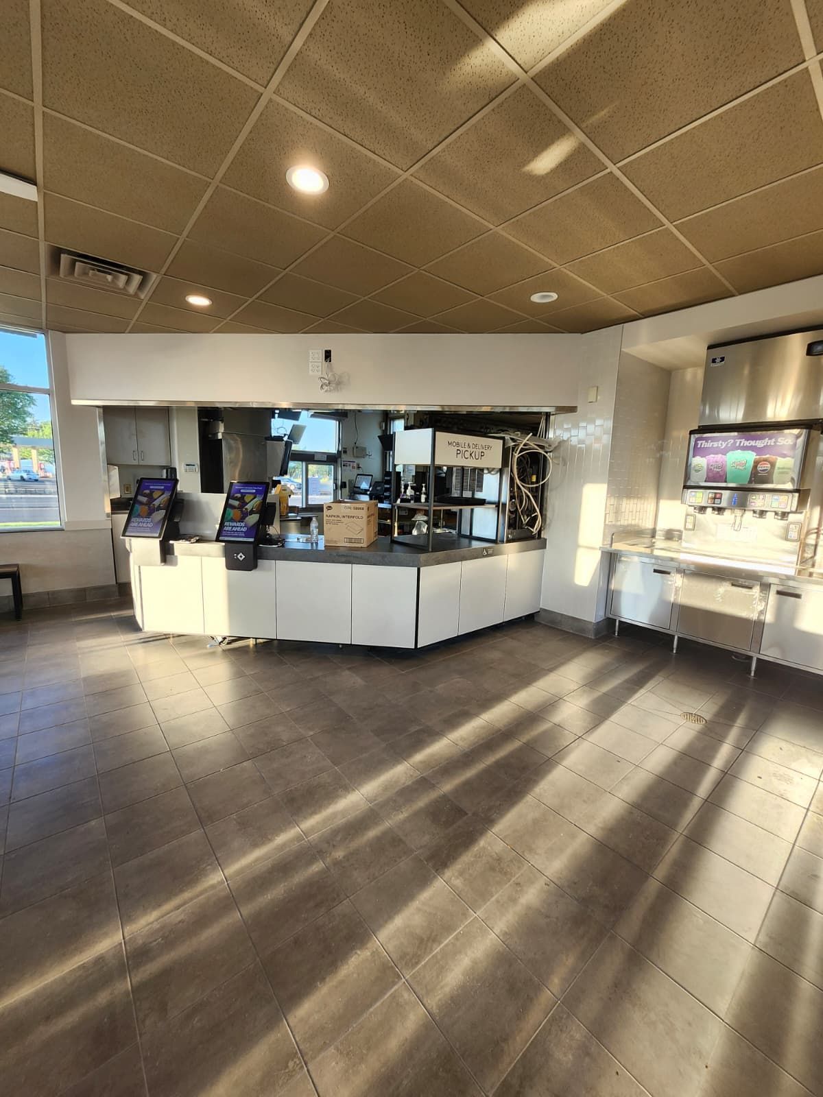 Empty modern café interior with white counter, menu screens, and bright sunlight on dark floor
