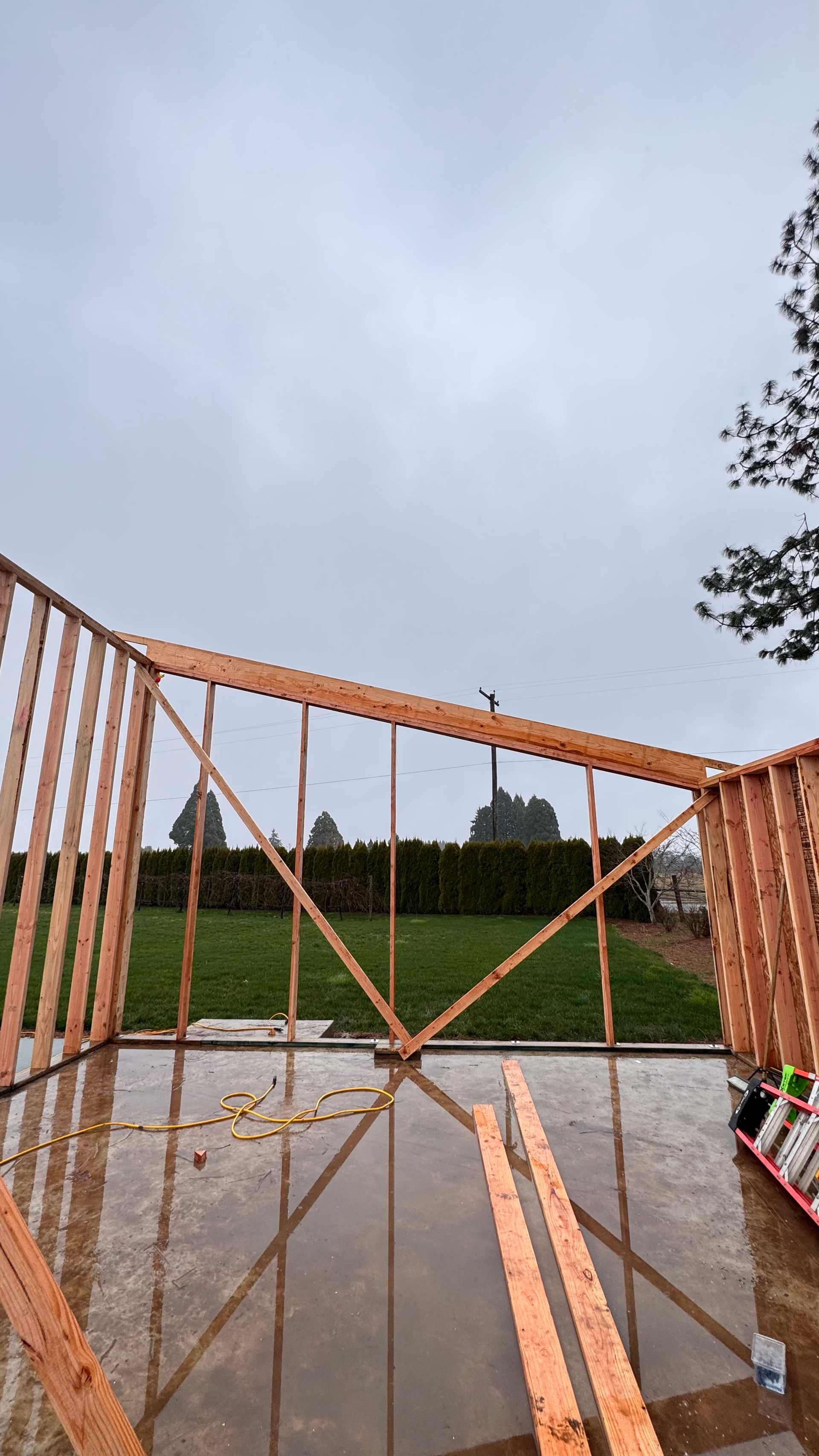 View from a wooden structure overlooking a wet patio, green field, and cloudy sky.