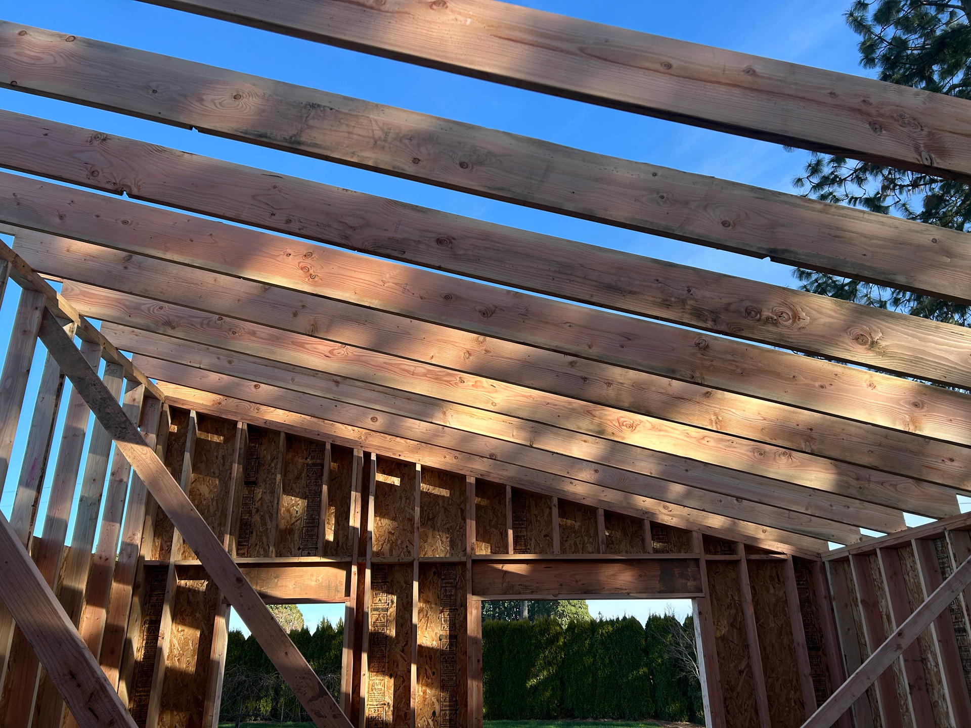 Framed wooden roof structure with exposed beams under a blue sky during construction