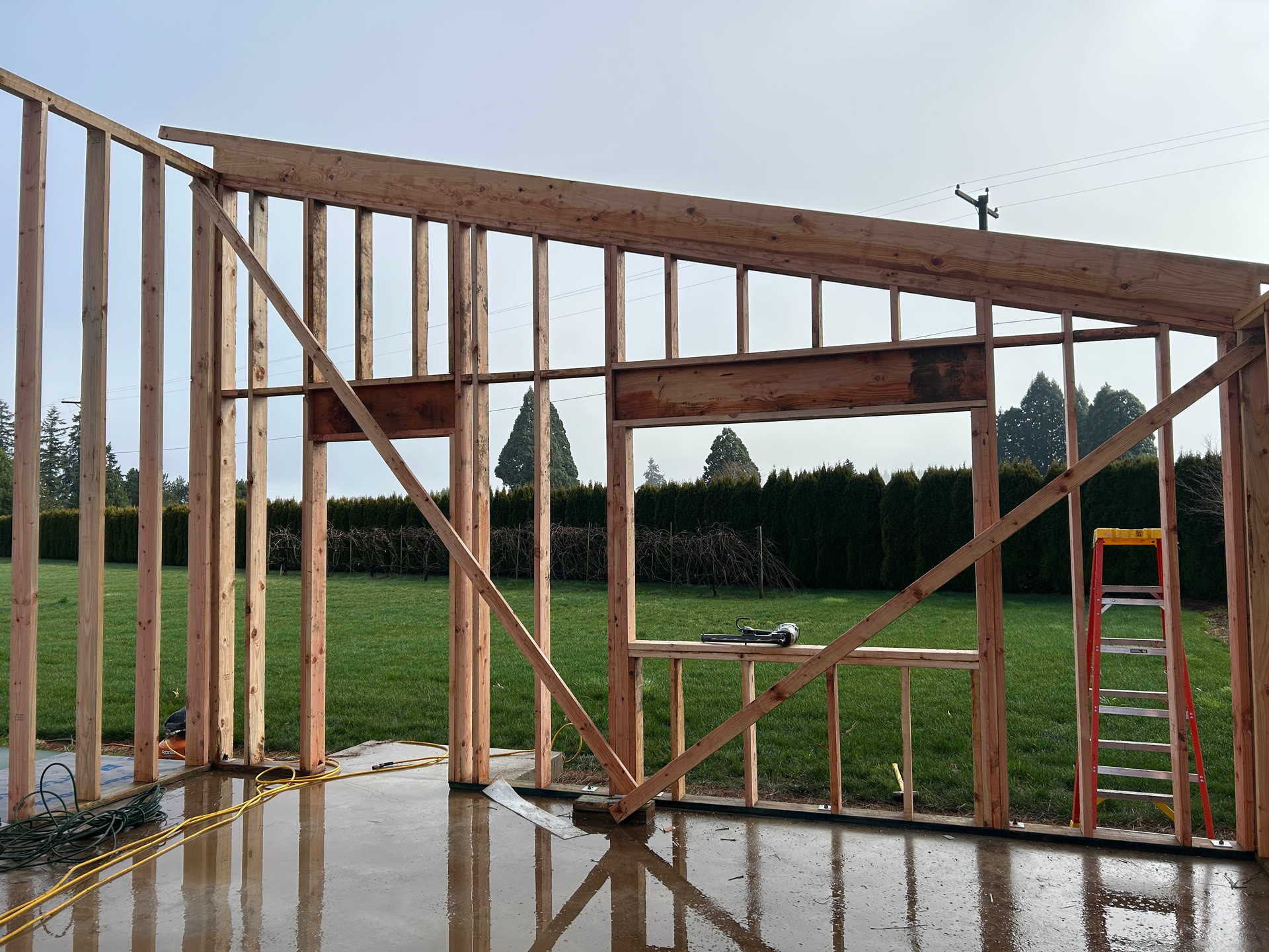 Rain-soaked wooden gate blocking a grassy field, with a dark fence and overcast sky beyond.