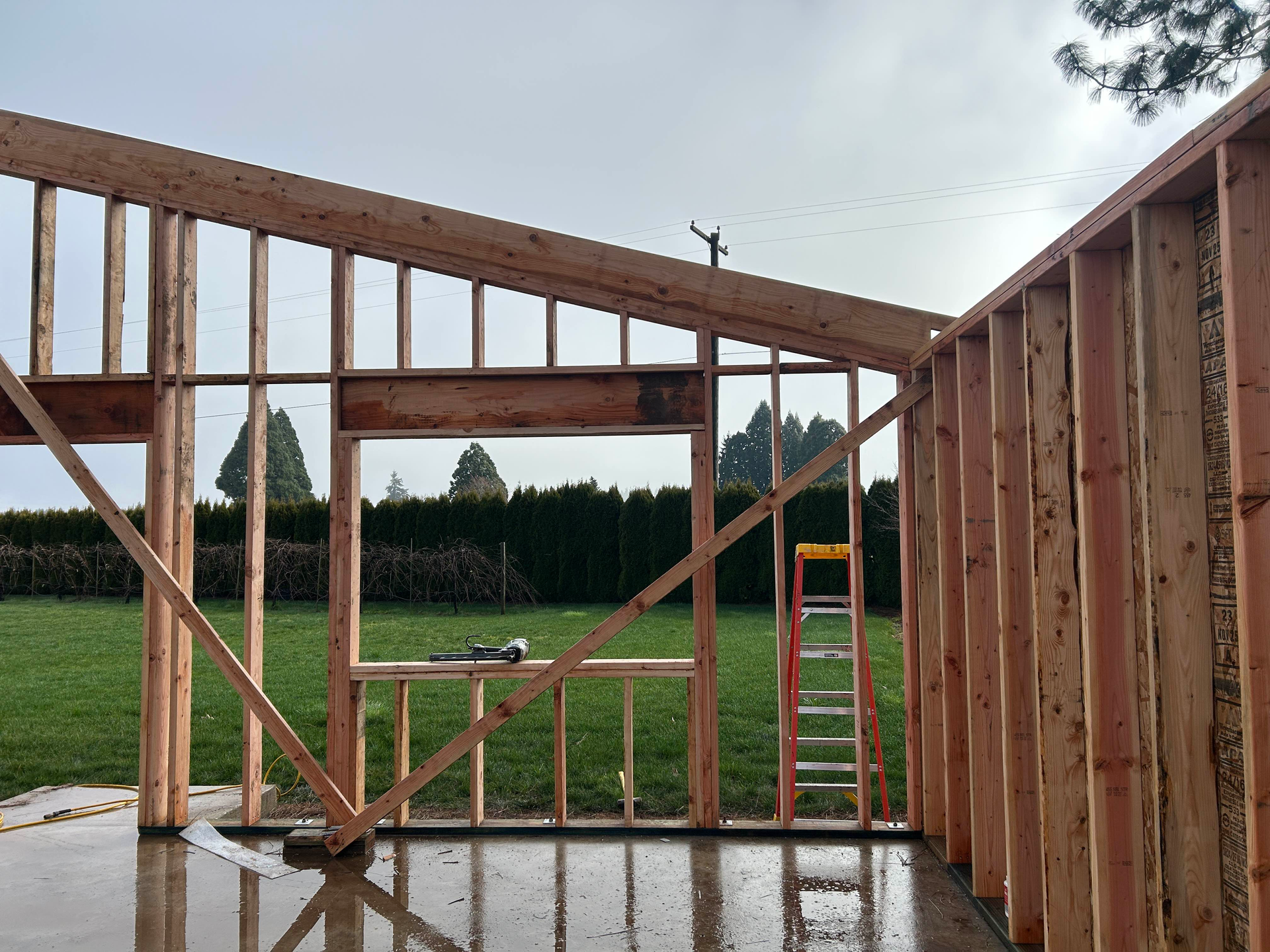 Partially framed wooden garage with open wall framing and a sloped roof on a concrete slab, facing a grassy yard