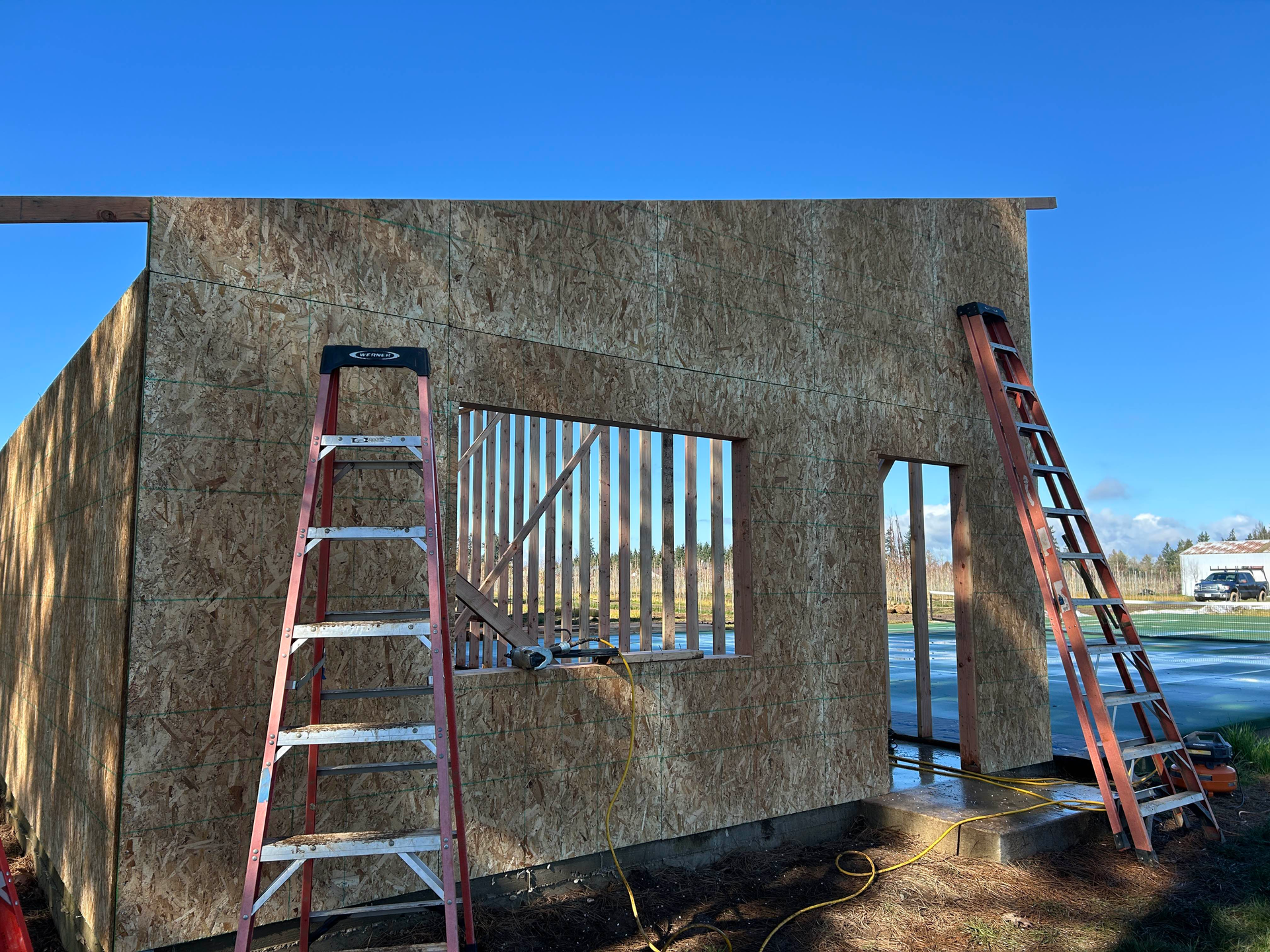 Partially built structure with ladders leaning against a stucco wall under a clear blue sky