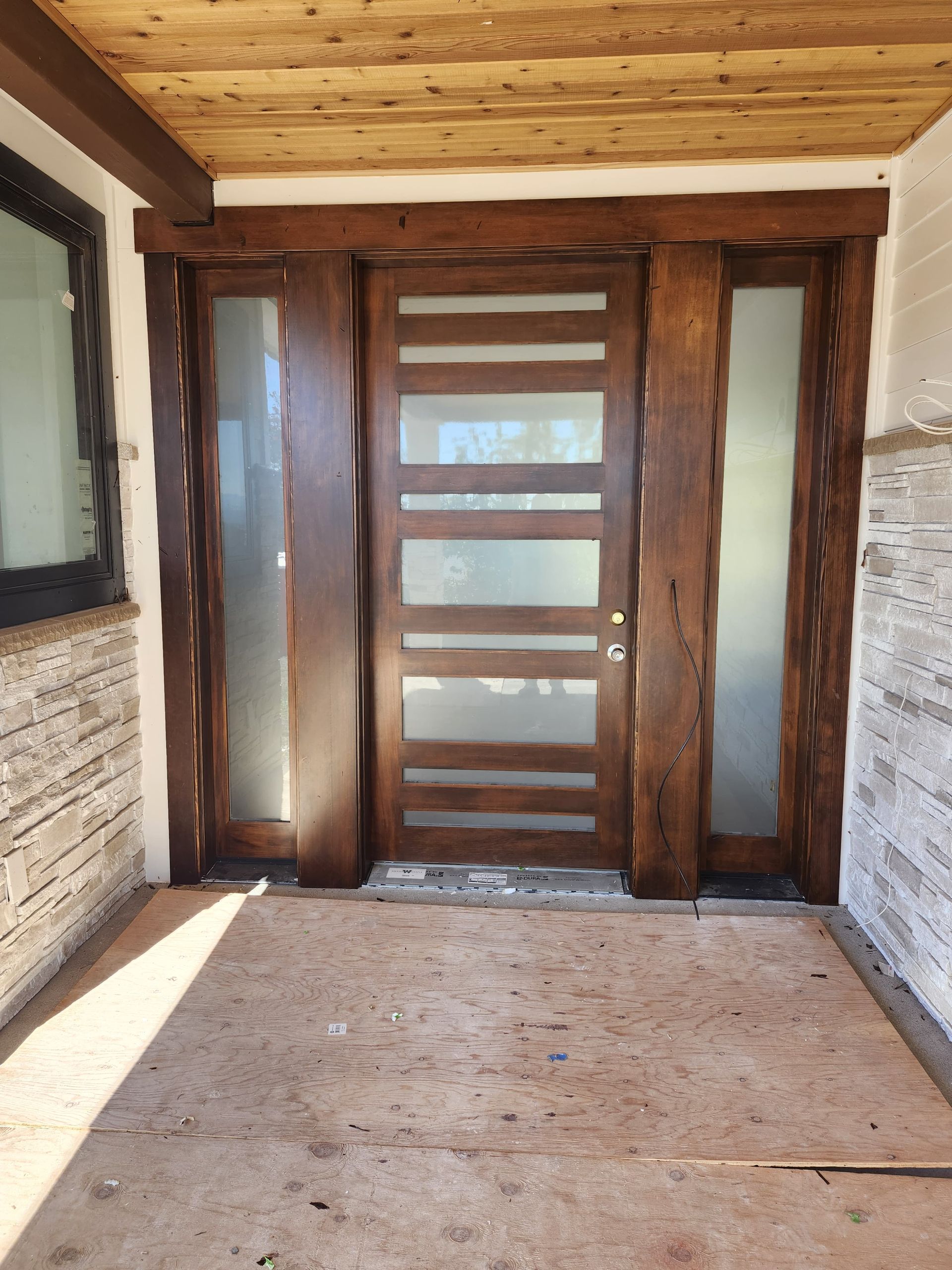 Wooden front entryway with glass-paneled door, stone walls, and covered porch ceiling