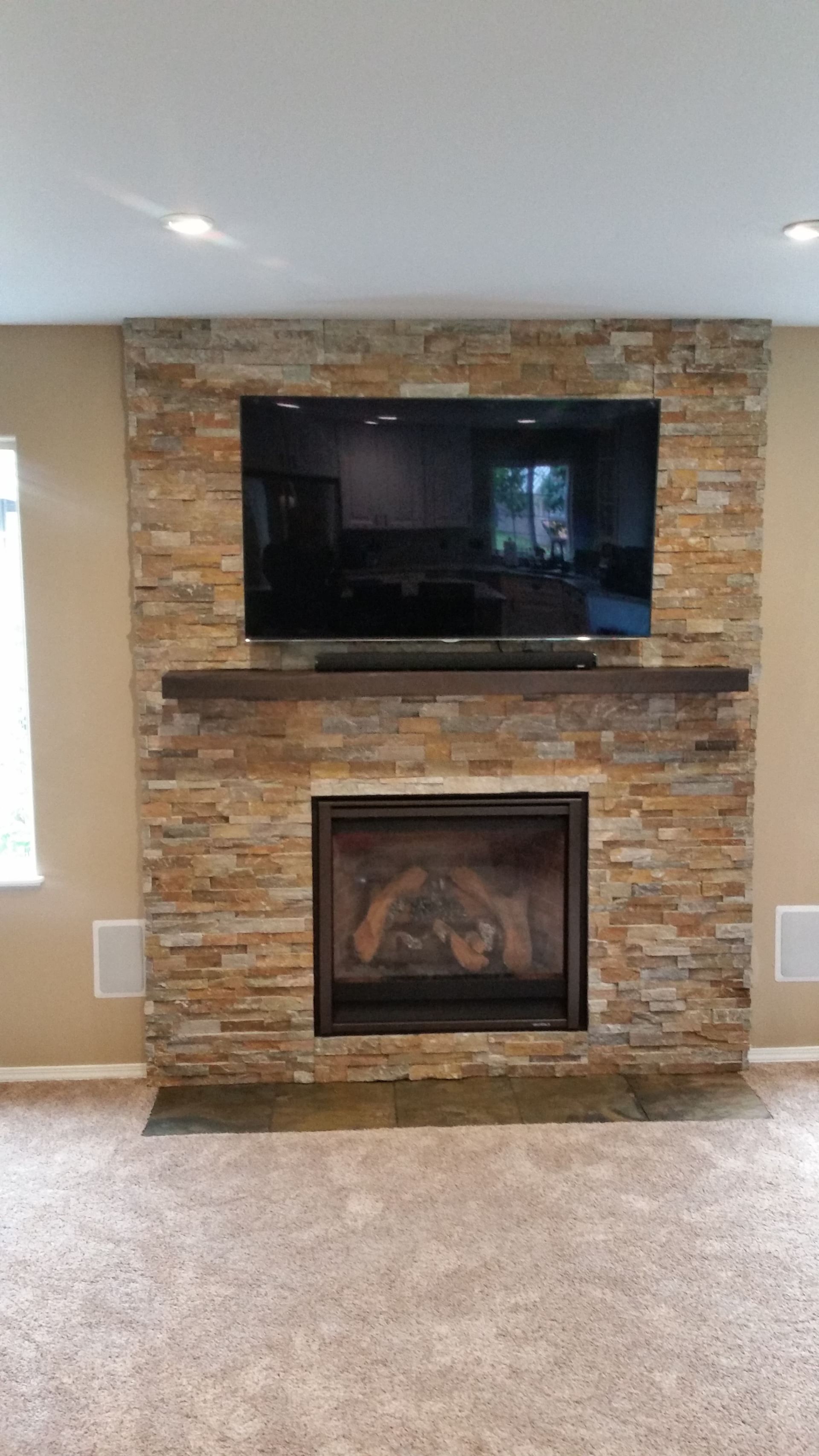 Stone fireplace with a wall-mounted TV above it in a carpeted living room.