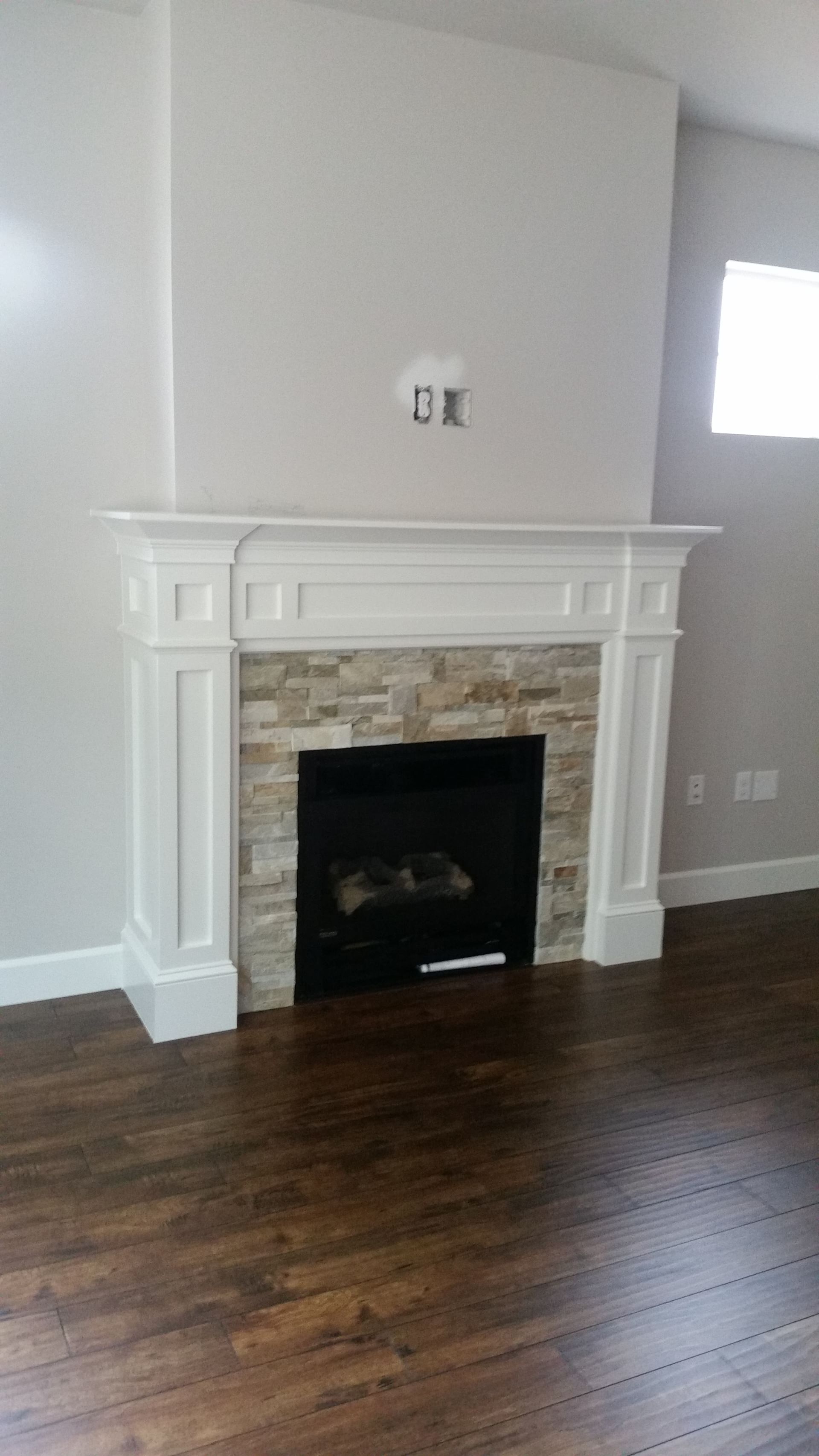 Empty living room with white fireplace mantel, stone surround, and dark hardwood floors.
