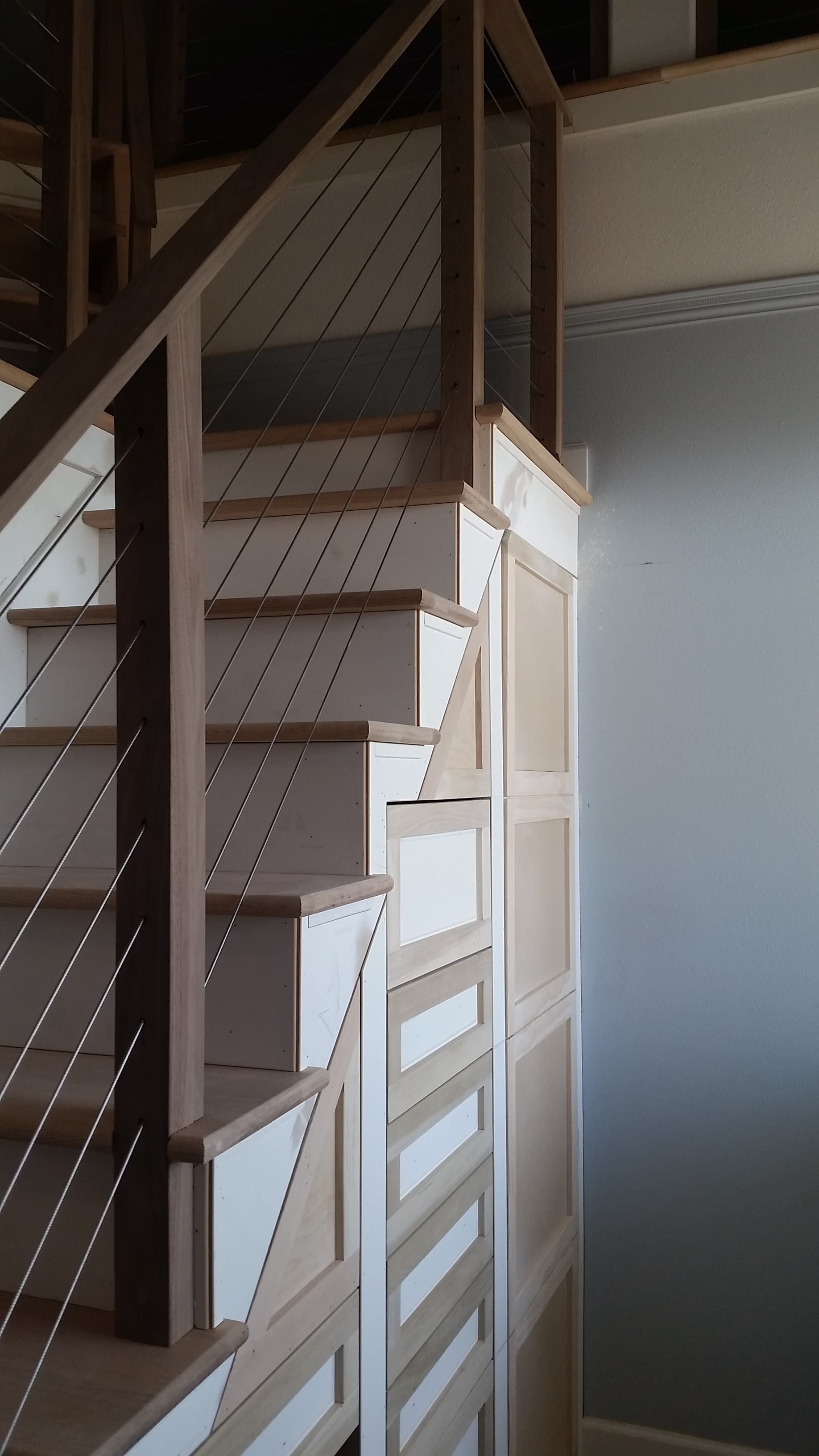 Indoor staircase with white and wood railing beside a wall and upper loft area
