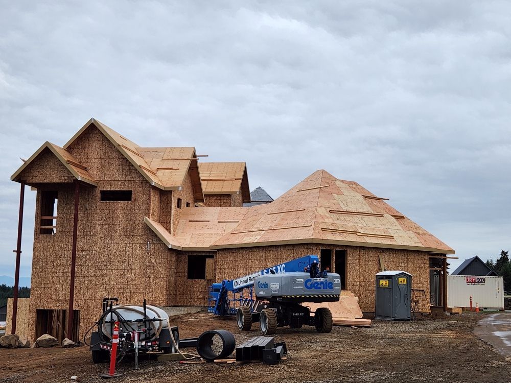 Partially built house under construction with roof framing, a blue lift, and a cloudy sky