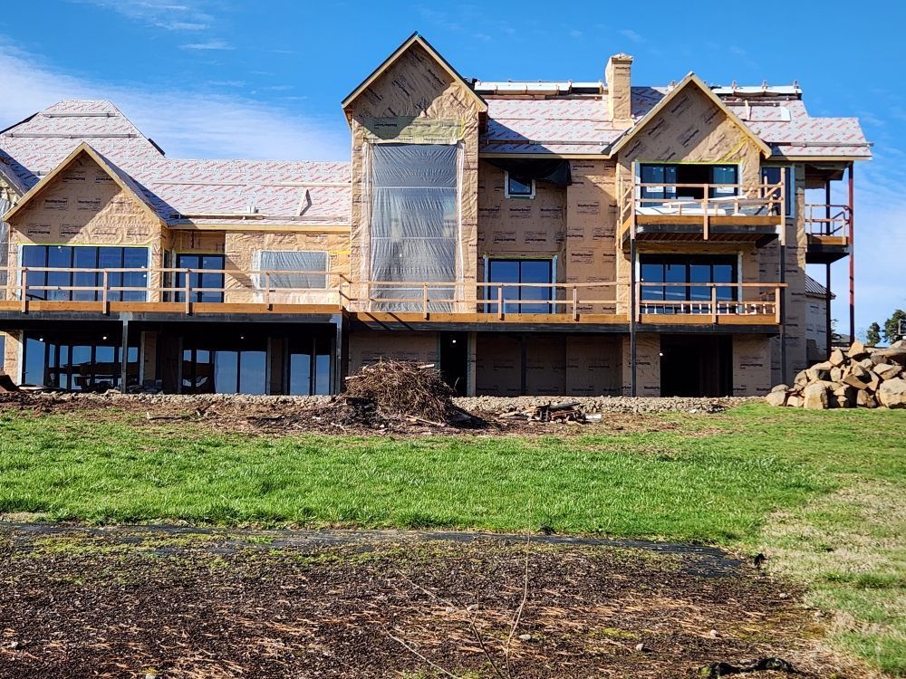 Partially finished house with wood siding and stone foundation on a grassy lot under a clear blue sky