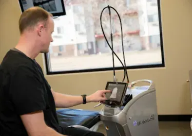 Man using medical equipment in a dental office. He points to a screen, window in background.