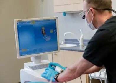 Dentist using a digital scanner to design a dental crown, blue gloves, monitor with teeth scan.