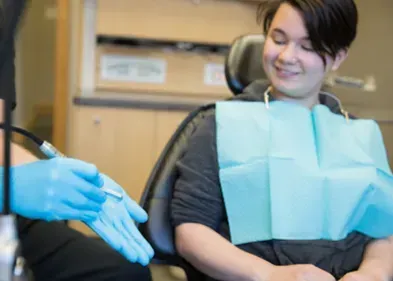 Dentist holding a tool, preparing to examine a patient sitting in a dental chair.