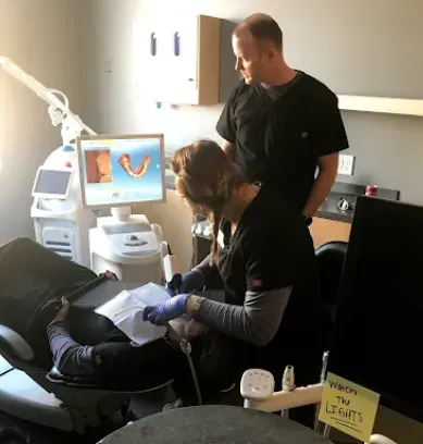 Dentists examining patient's teeth in a dental office. One dentist looks at the screen displaying a tooth scan.