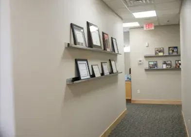 Hallway with framed documents on floating shelves, carpeted floor, and exit sign.