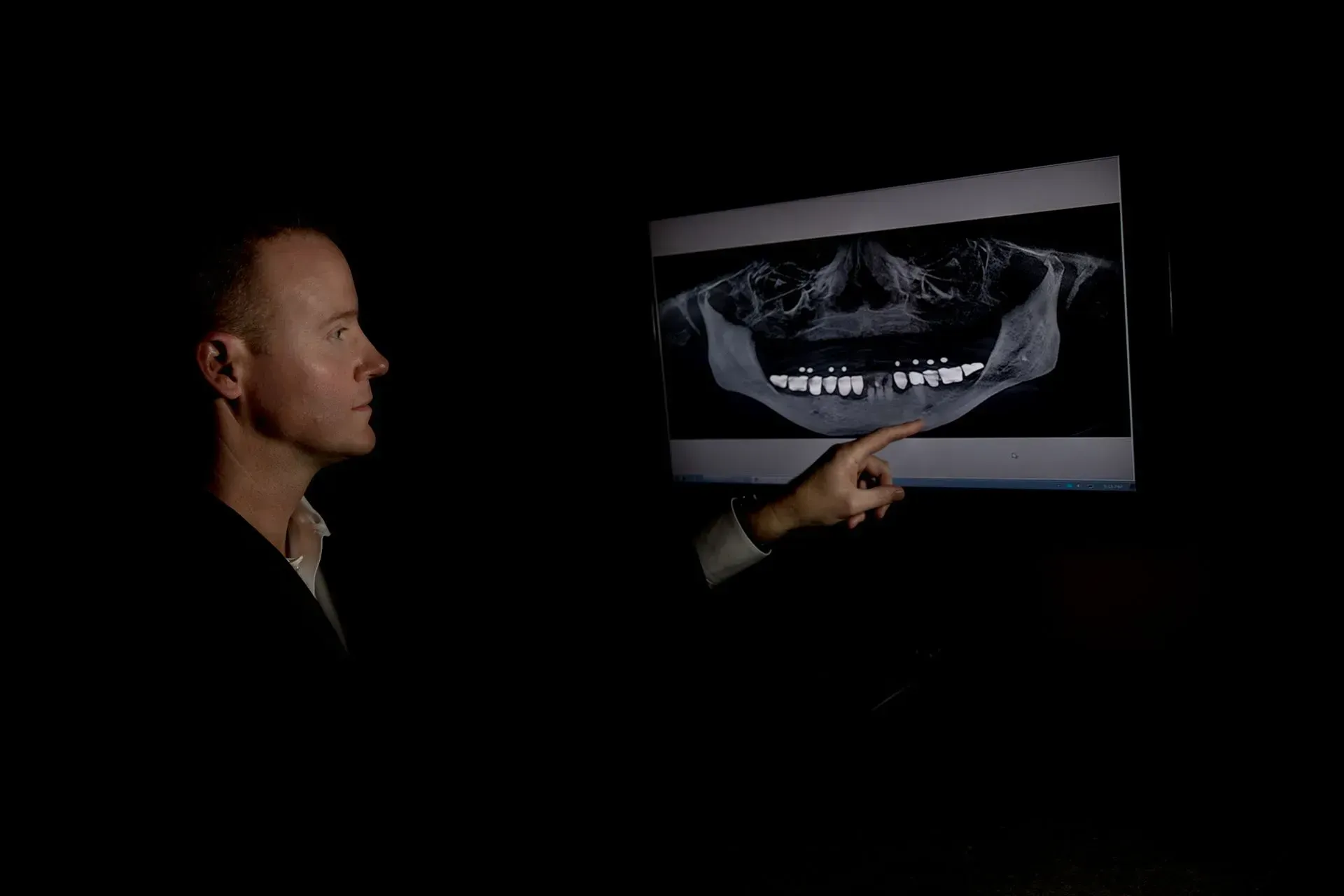 Man points to a dental x-ray on a monitor in a dark room.
