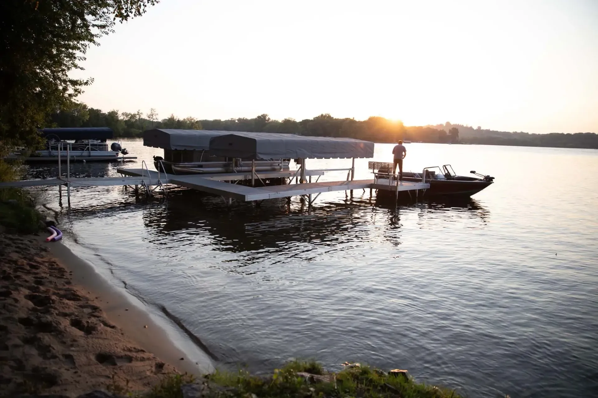 Docks on calm water at sunset, a person stands on a dock by a boat.
