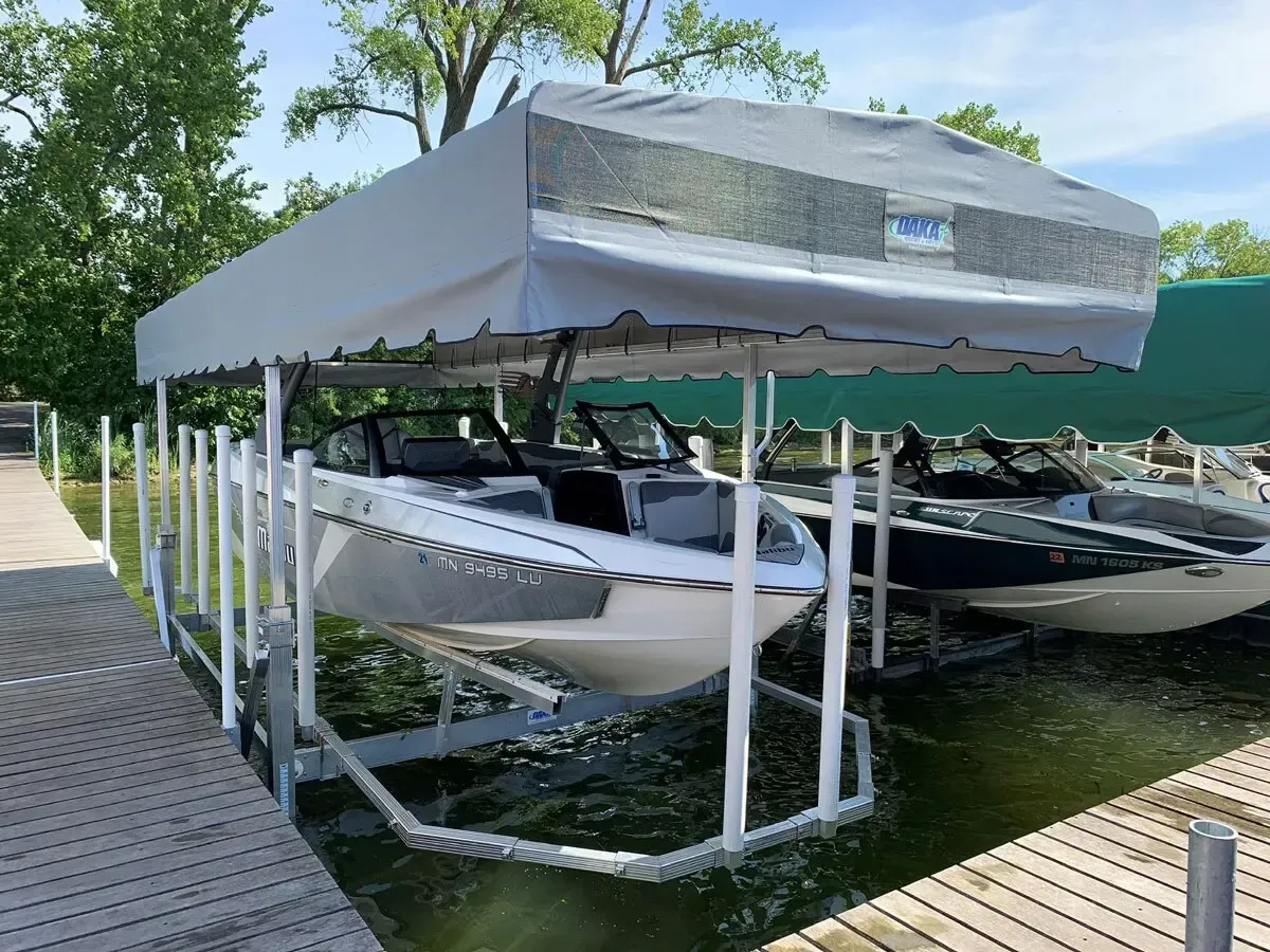 Boat on a lift under a white canopy on a dock, other boats visible.