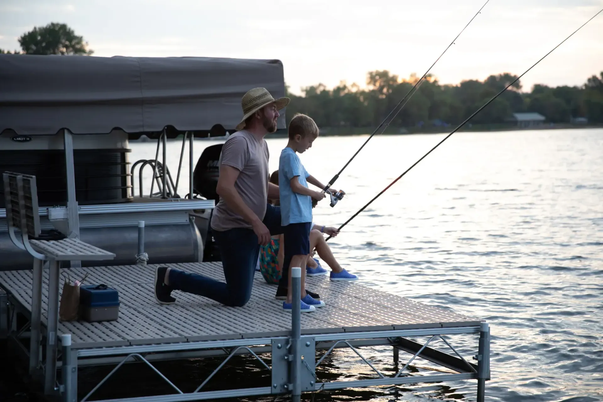 Father and child fishing on a dock at dusk, rods cast into the water.