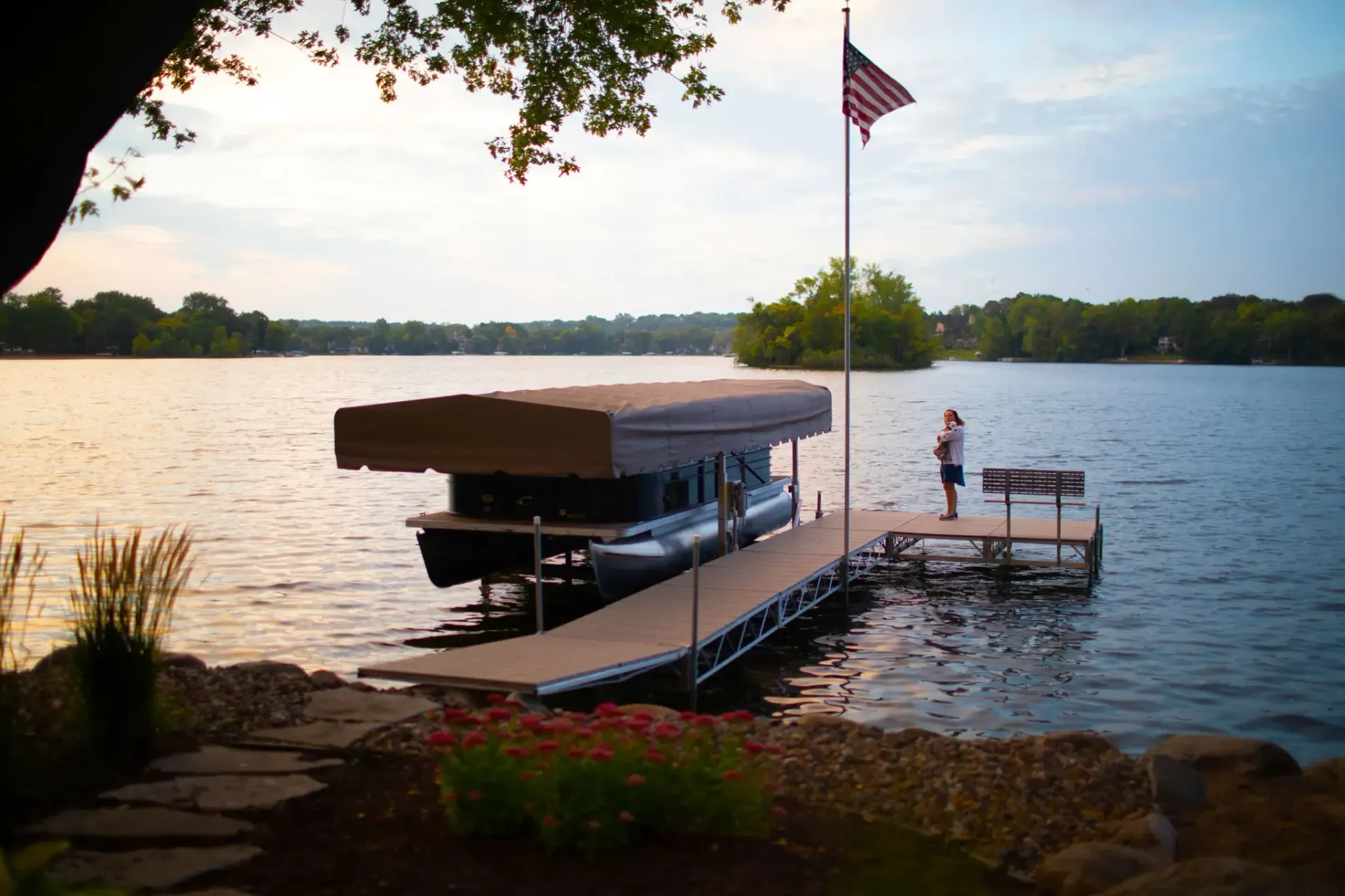 Dock on a lake with a boat, American flag, and person standing. Cloudy sky.