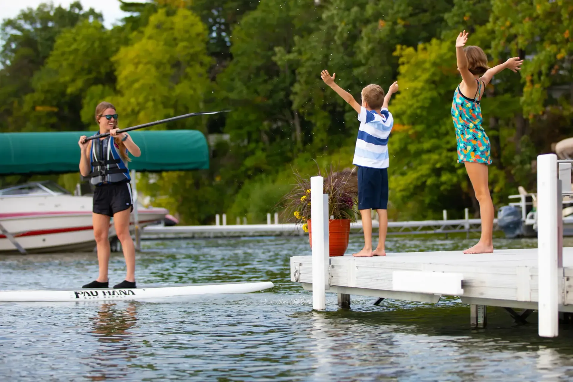 Woman waterskiing on a lake, watched by two children on a dock, arms raised in excitement.