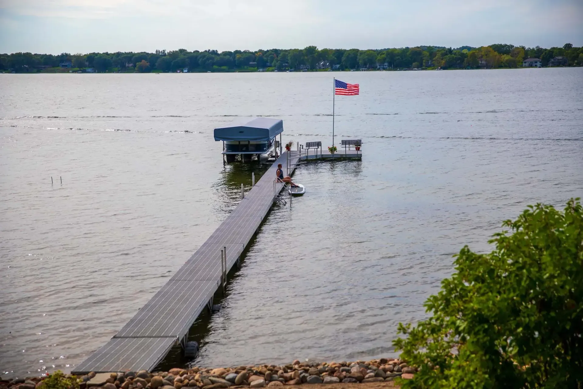 Long pier with solar panels leading to a dock on a lake; flag on the dock.