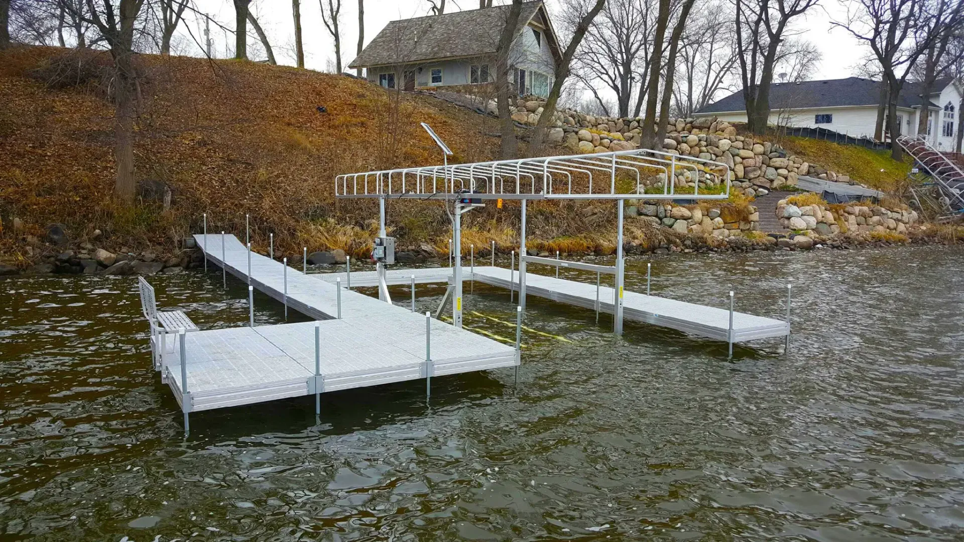 Dock extending into water, with a metal structure, and a house on the hill in the background.