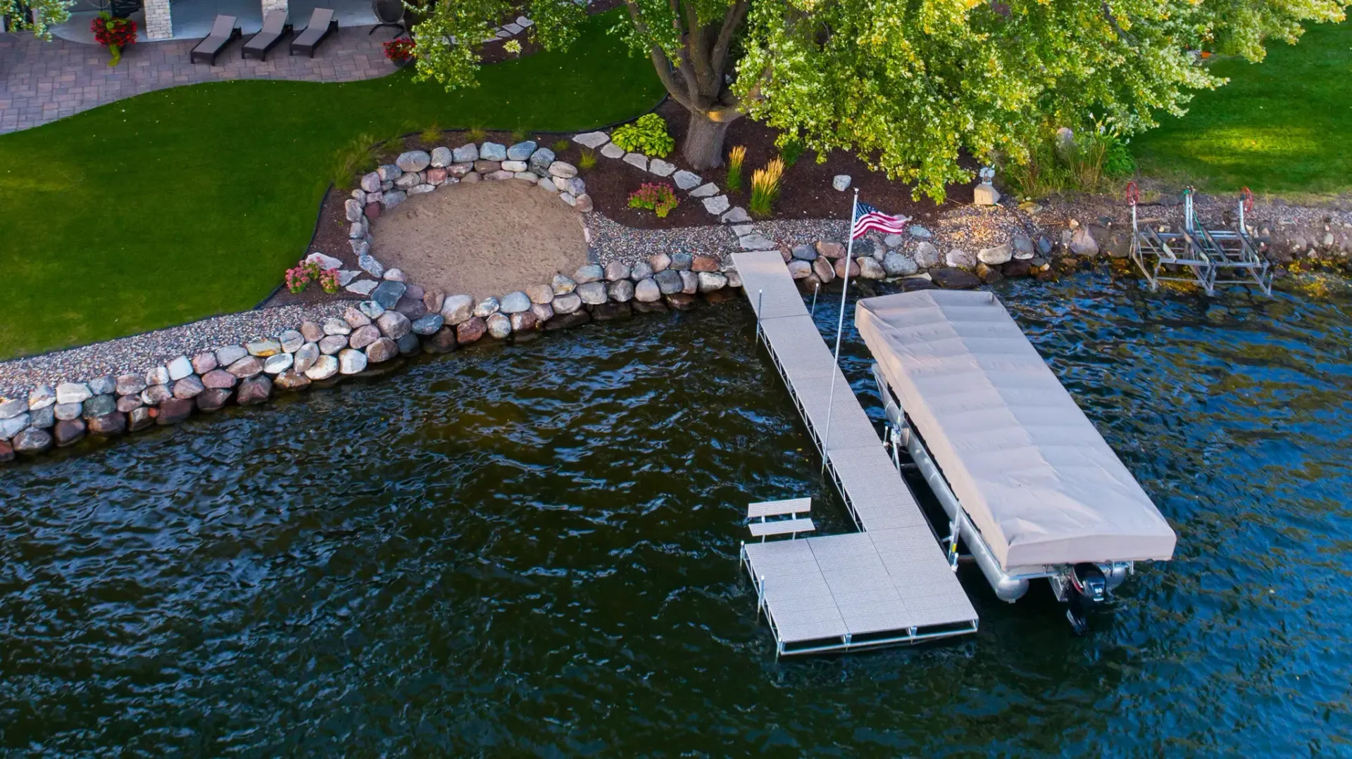 Dock on a lake with a covered boat lift, surrounded by shoreline rocks and greenery.