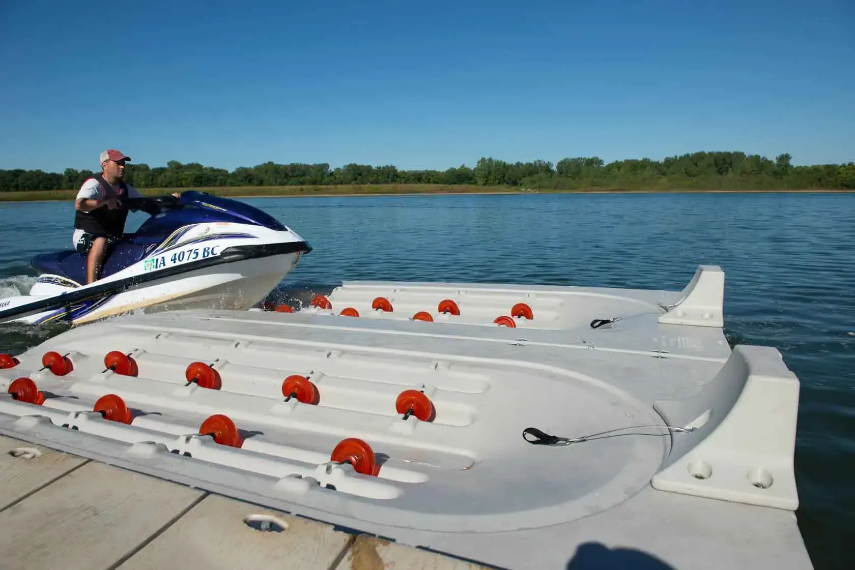 Jet ski approaching a white floating dock with red rollers on a sunny lake.