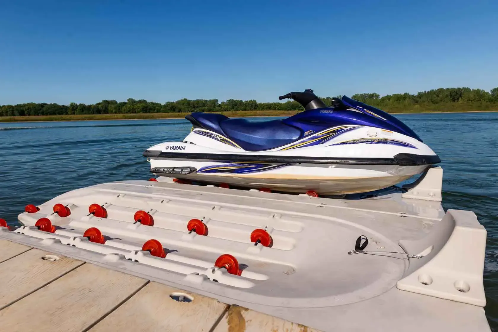 Jet ski on a white and gray floating dock with red rollers, blue sky and water background.