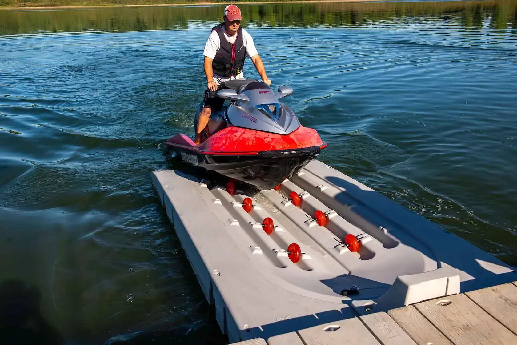 Man on a red jet ski, pulling onto a gray floating dock with red rollers.