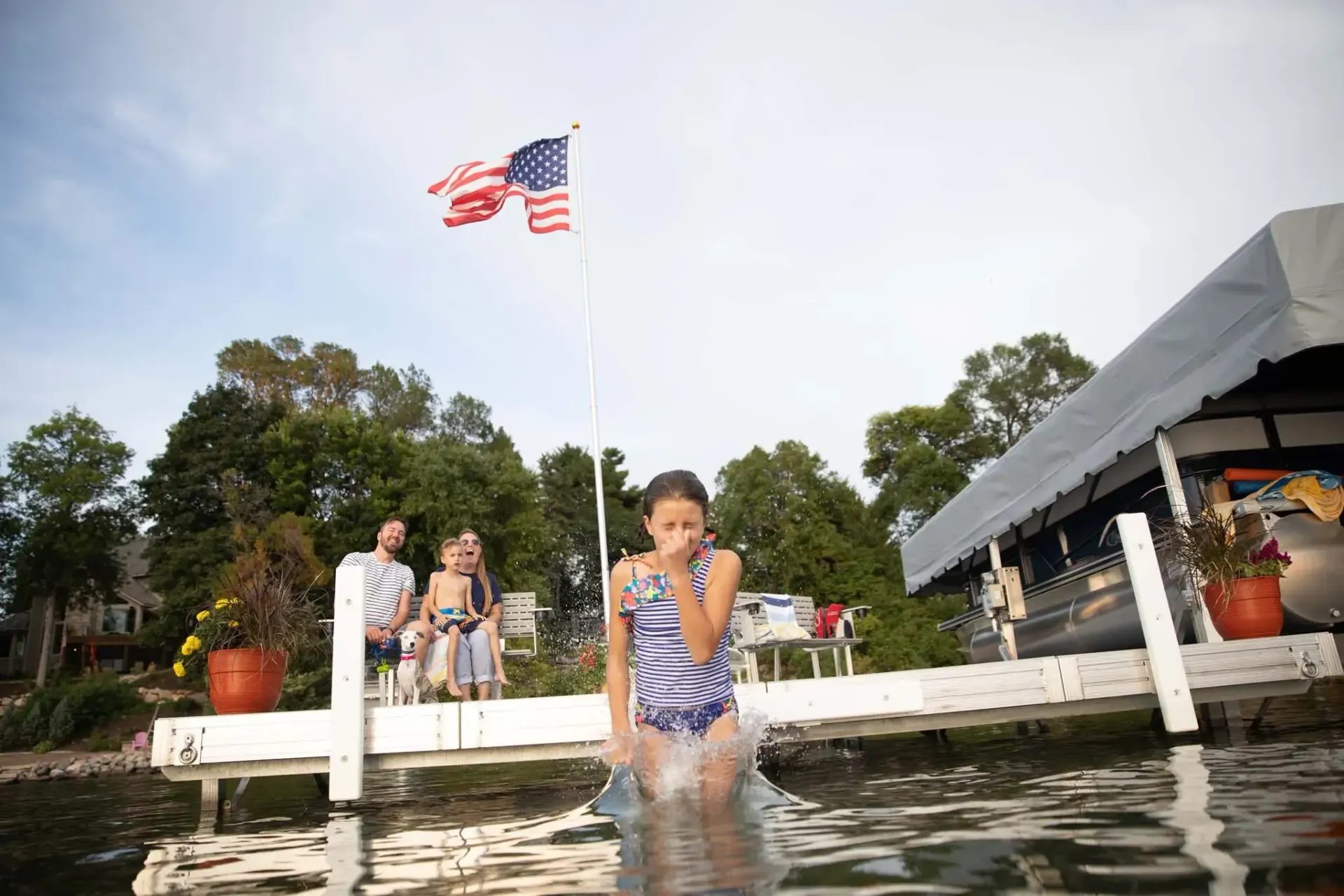 Girl emerges from water on a dock; family watches under an American flag.