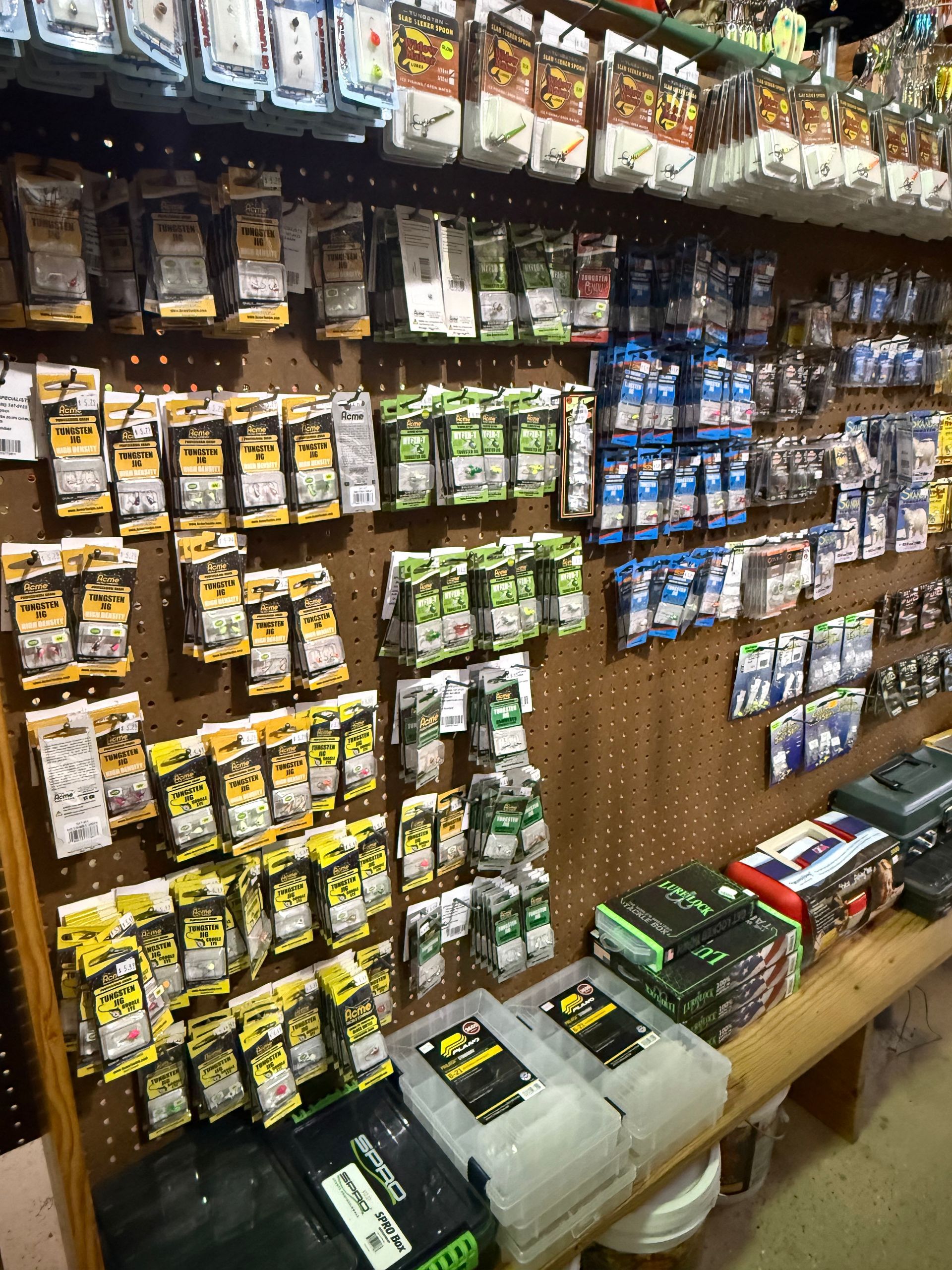 Fishing tackle display: various packaged hooks, lures, and supplies arranged on a pegboard wall in a store setting.
