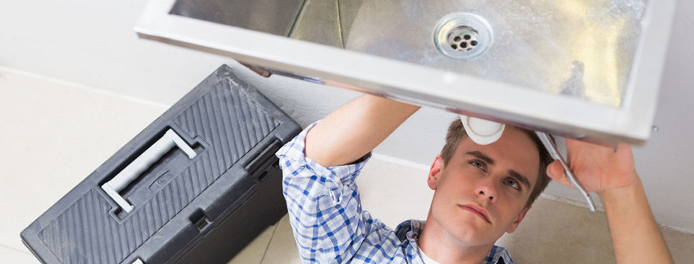 Technician checking under-sink plumbing with toolbox nearby