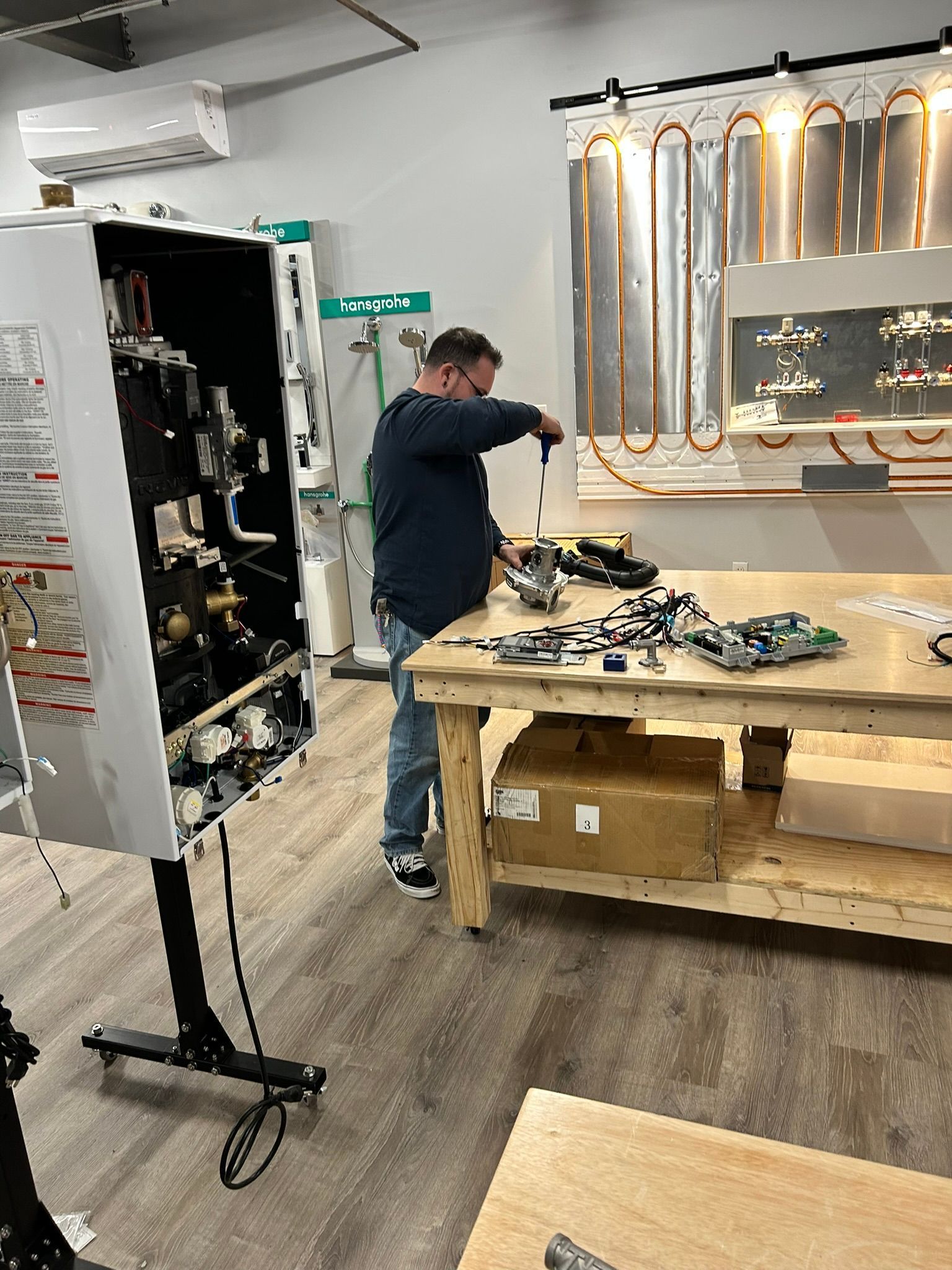 Technician working on an open electronics cabinet in a workshop, with tools and parts on a workbench.