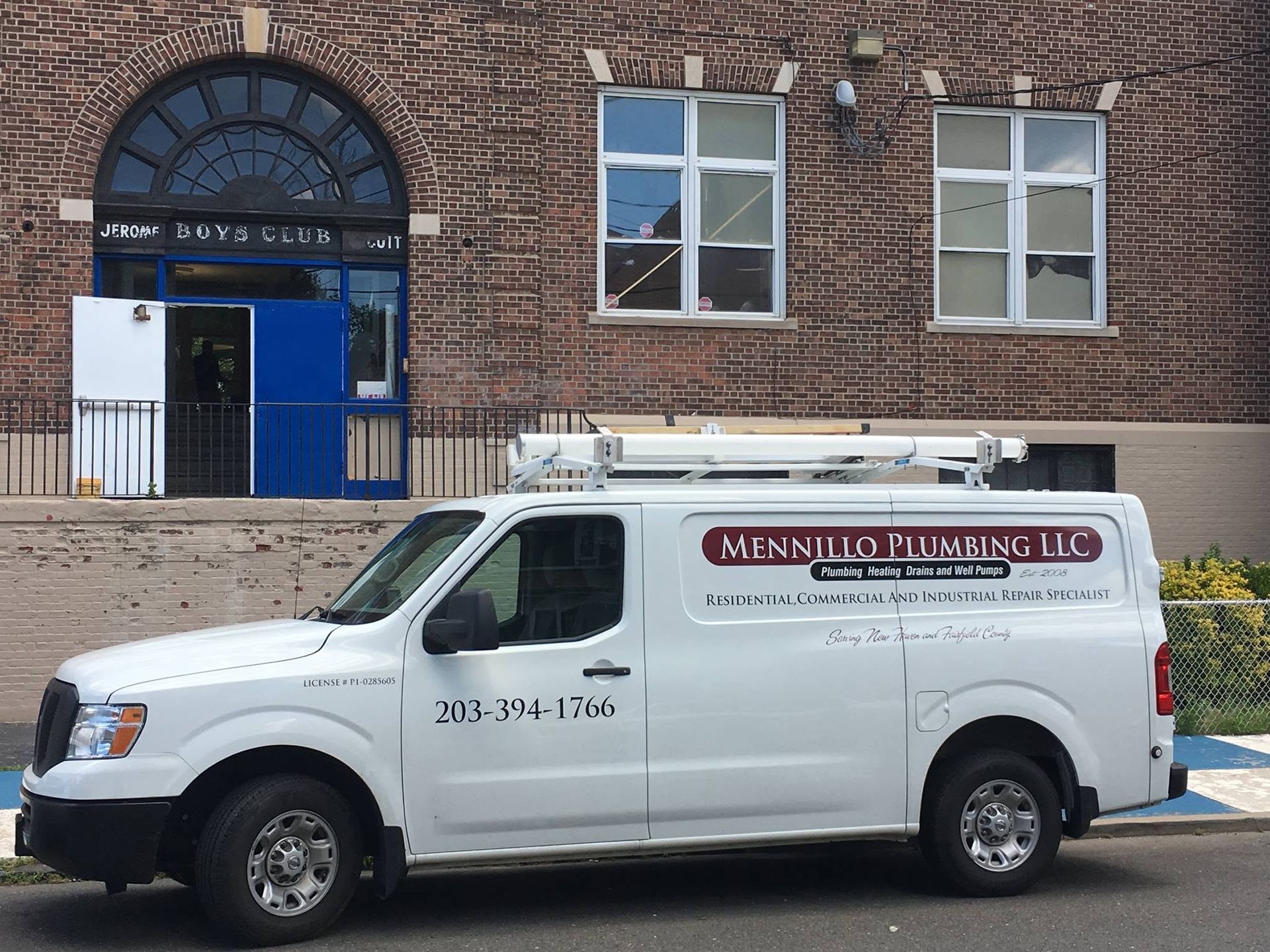 White plumbing service van parked in front of a brick building with blue doors and windows