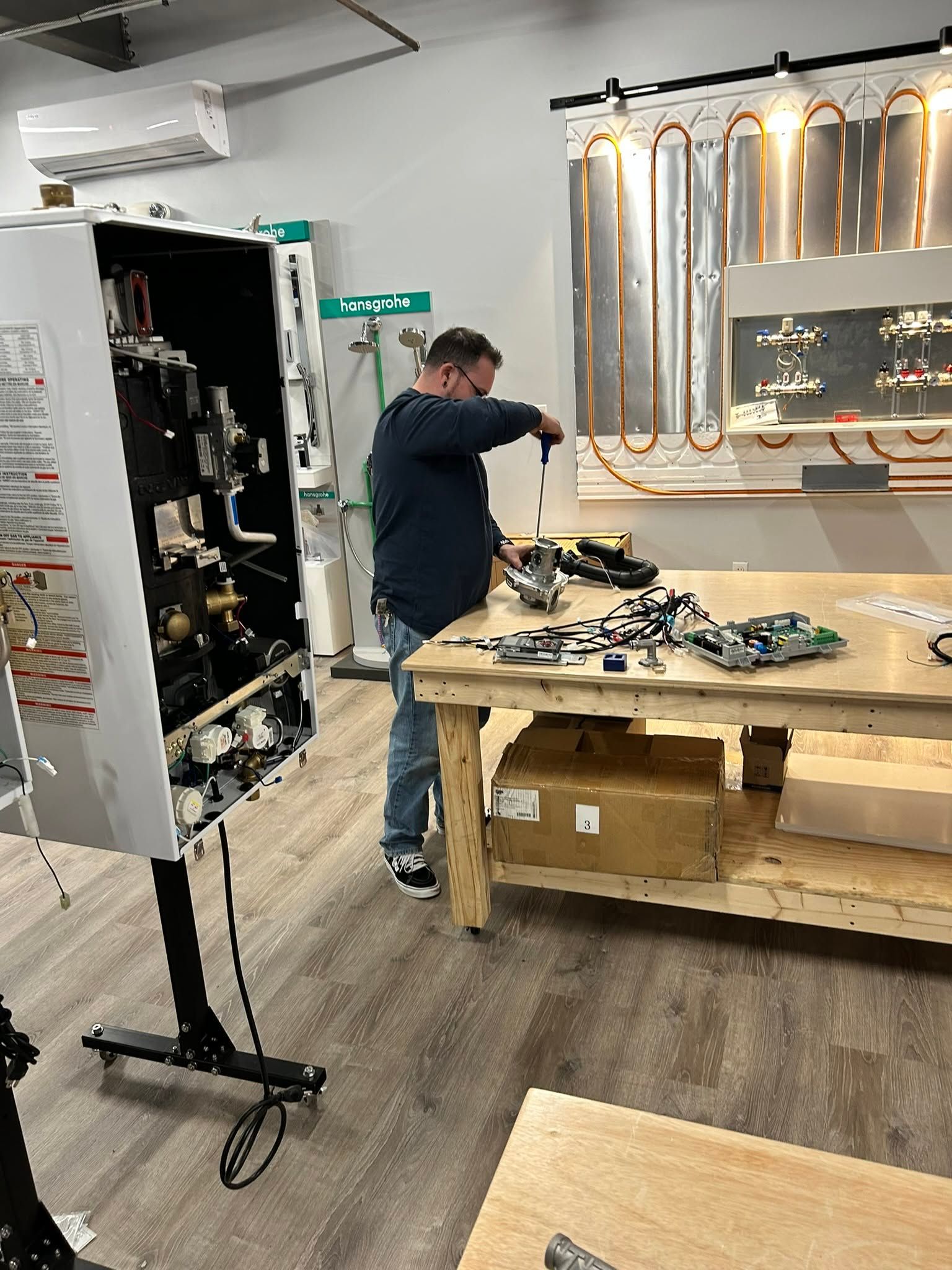 Person working on a wall-mounted display of coiled copper tubing in a workshop.