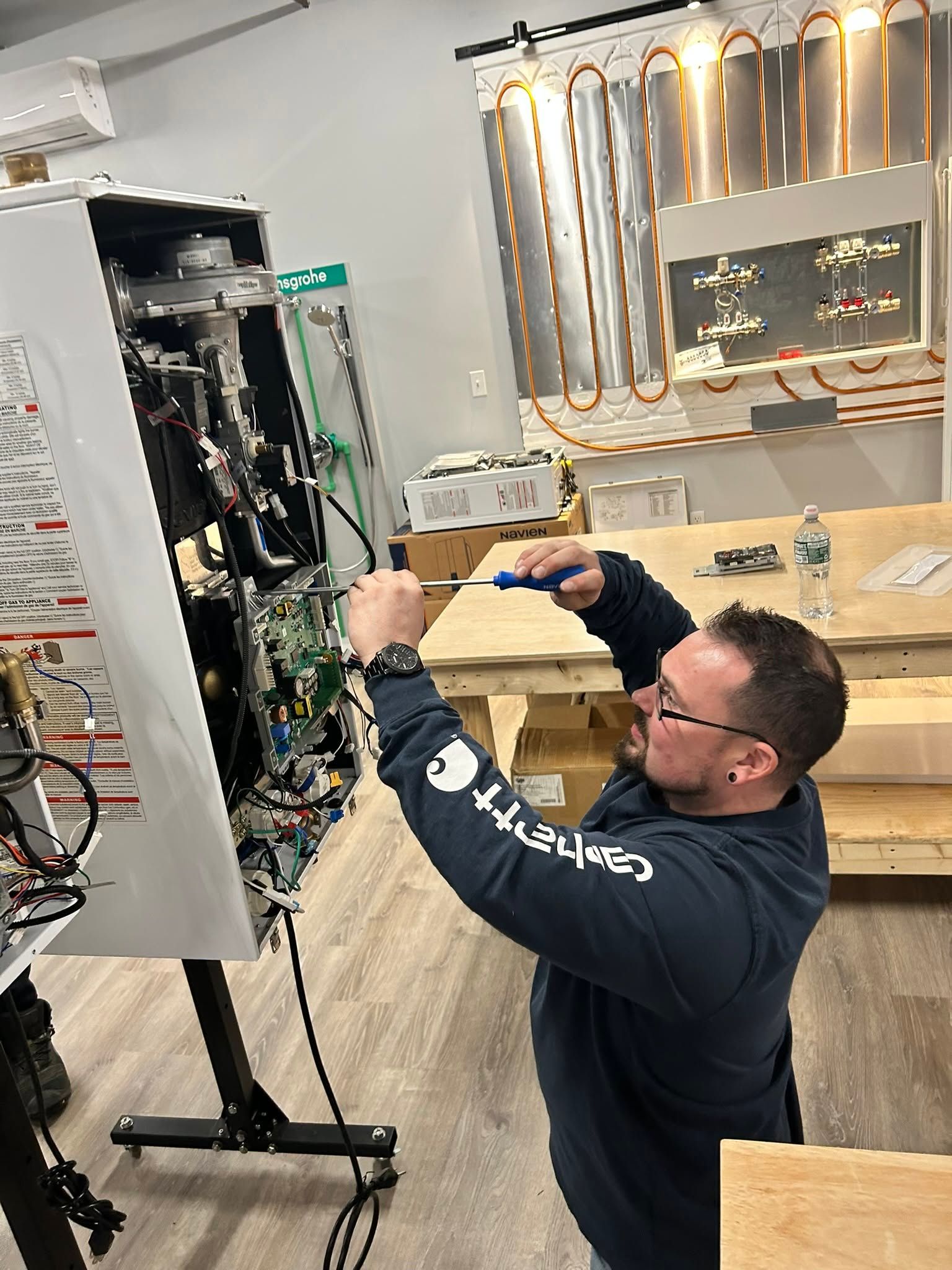 Technician adjusting wiring inside an open electrical panel in a workshop, with copper tubing on the wall.