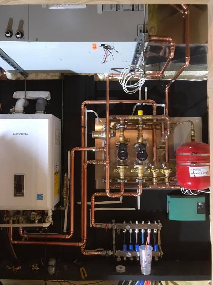 Boiler room with copper pipes, valves, a wall-mounted boiler, and a red expansion tank on a dark wall