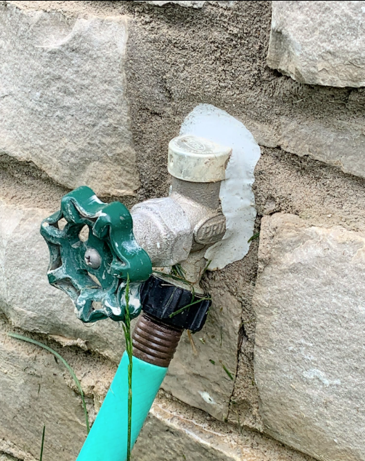 Green garden hose faucet with a white shutoff valve mounted on a stone wall